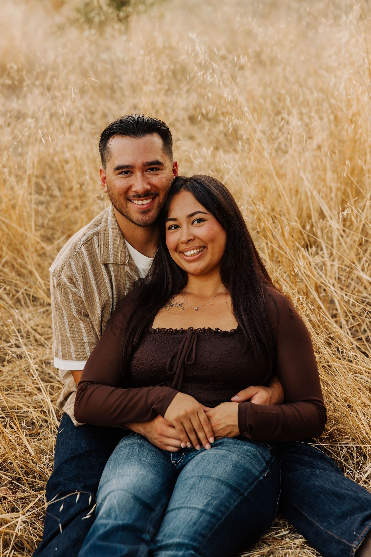Couple sitting together in golden grass during sunset photo session.