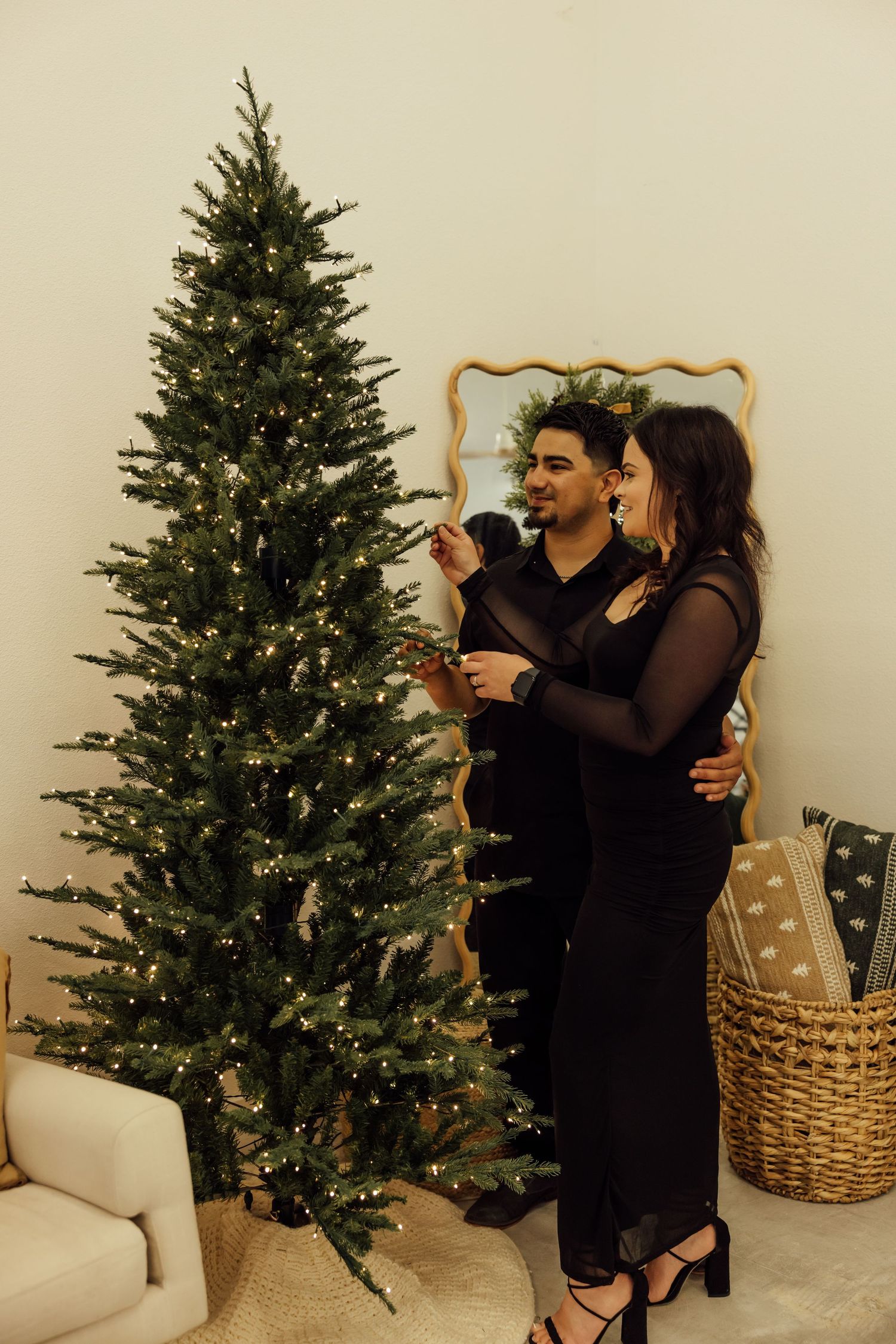 Couple sharing intimate moments near a lit Christmas tree in a minimalist setting.