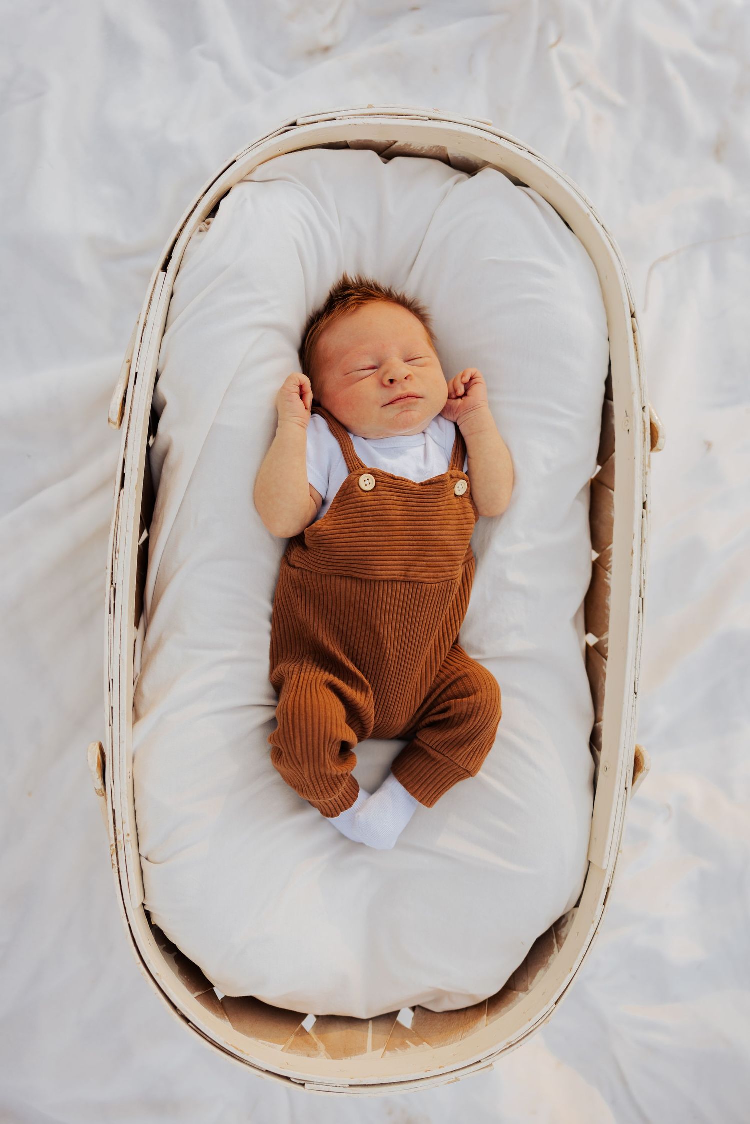 Sleeping infant in brown romper lying peacefully in white basket.