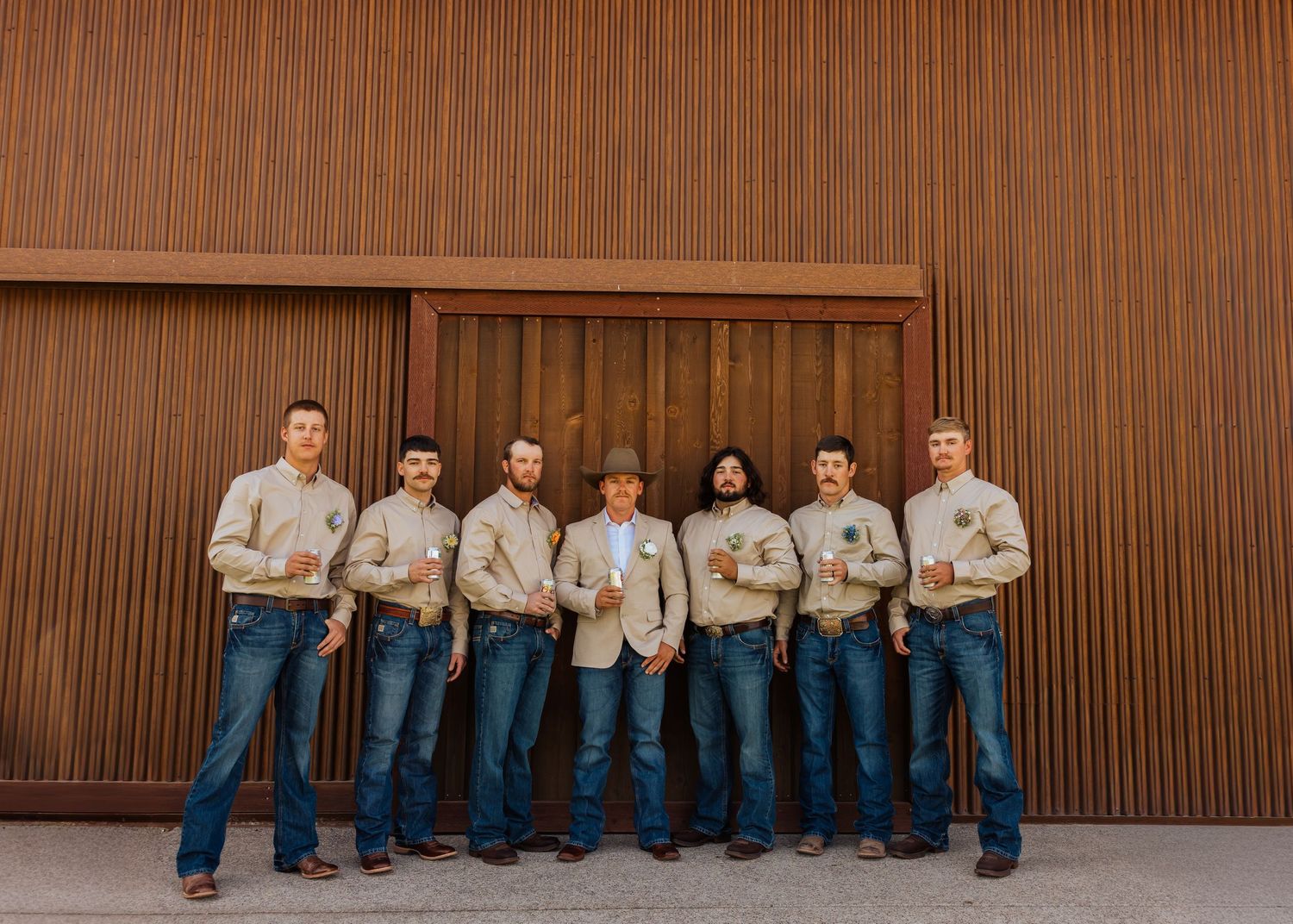 A group in matching western attire poses against a wooden wall for a wedding party photo.