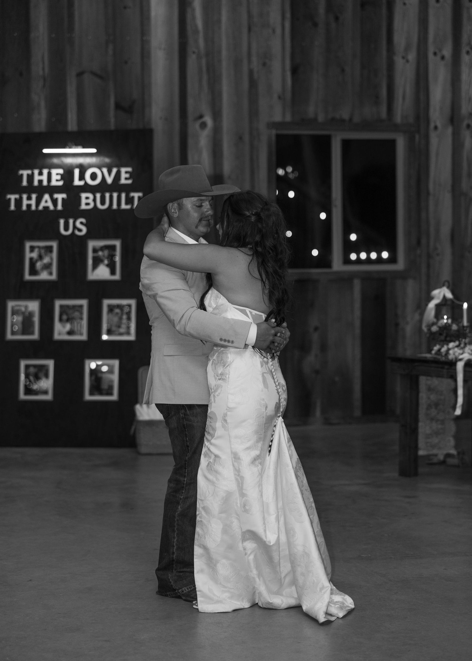 A romantic first dance at a rustic barn wedding with a lit sign reading 'The Love That Built Us' in the background.
