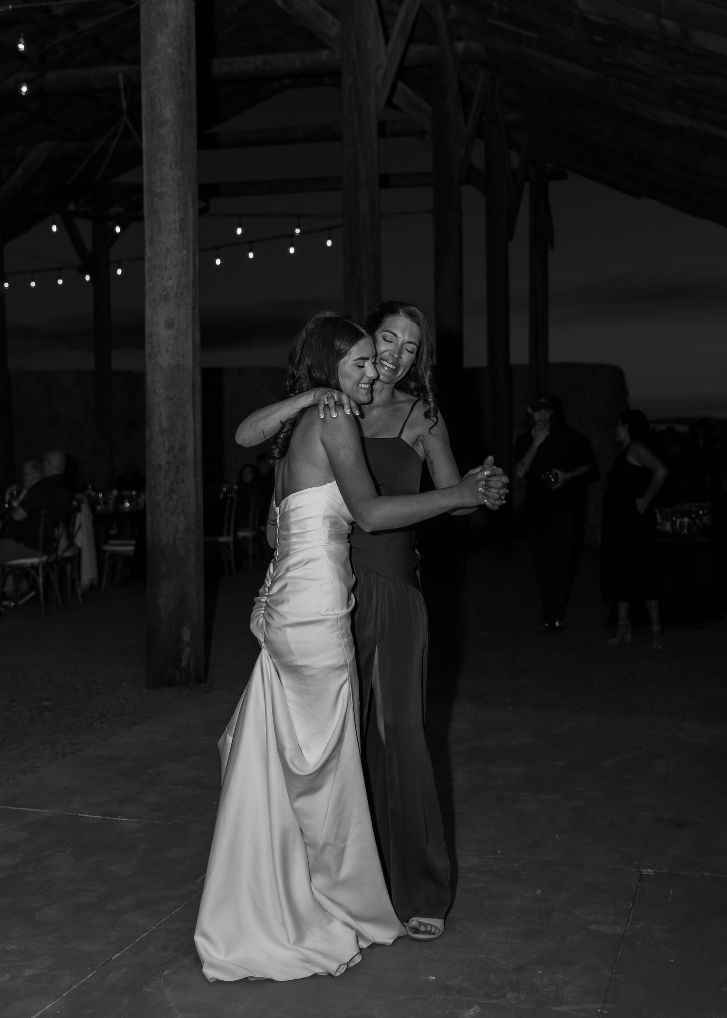 Wedding couple dancing under string lights in dark rustic barn venue.