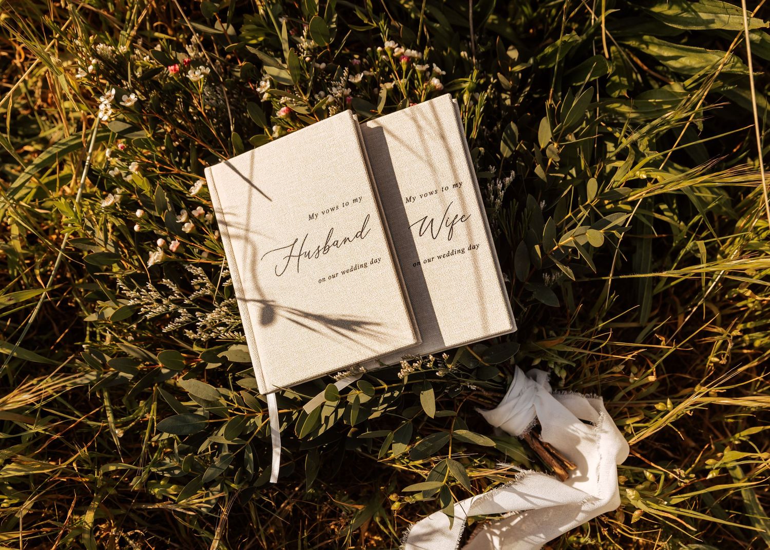 A wedding vow book labeled 'Husband' lies in golden grass with natural lighting.