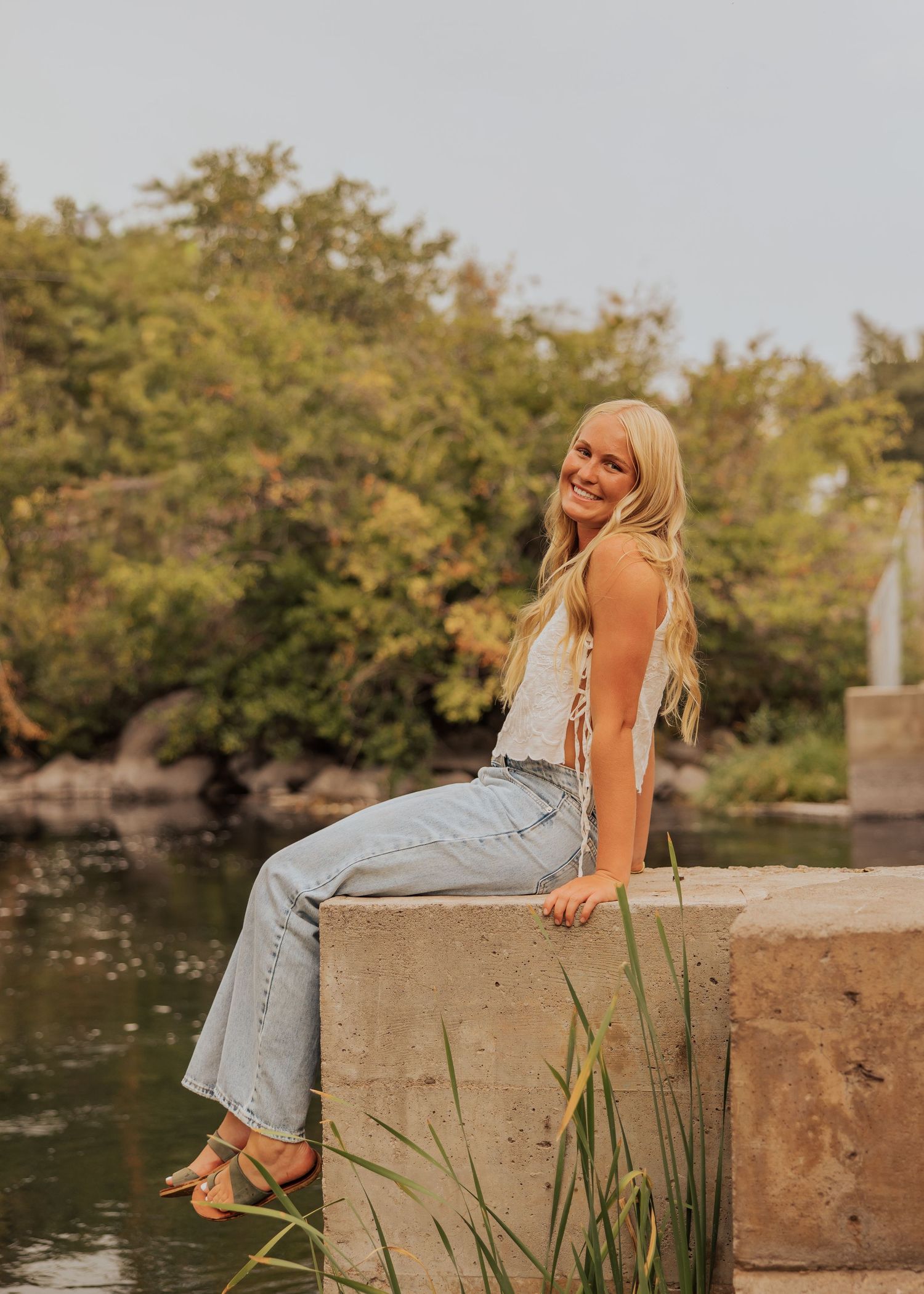 Artistic portraits by a lake with concrete wall and cattails in background.