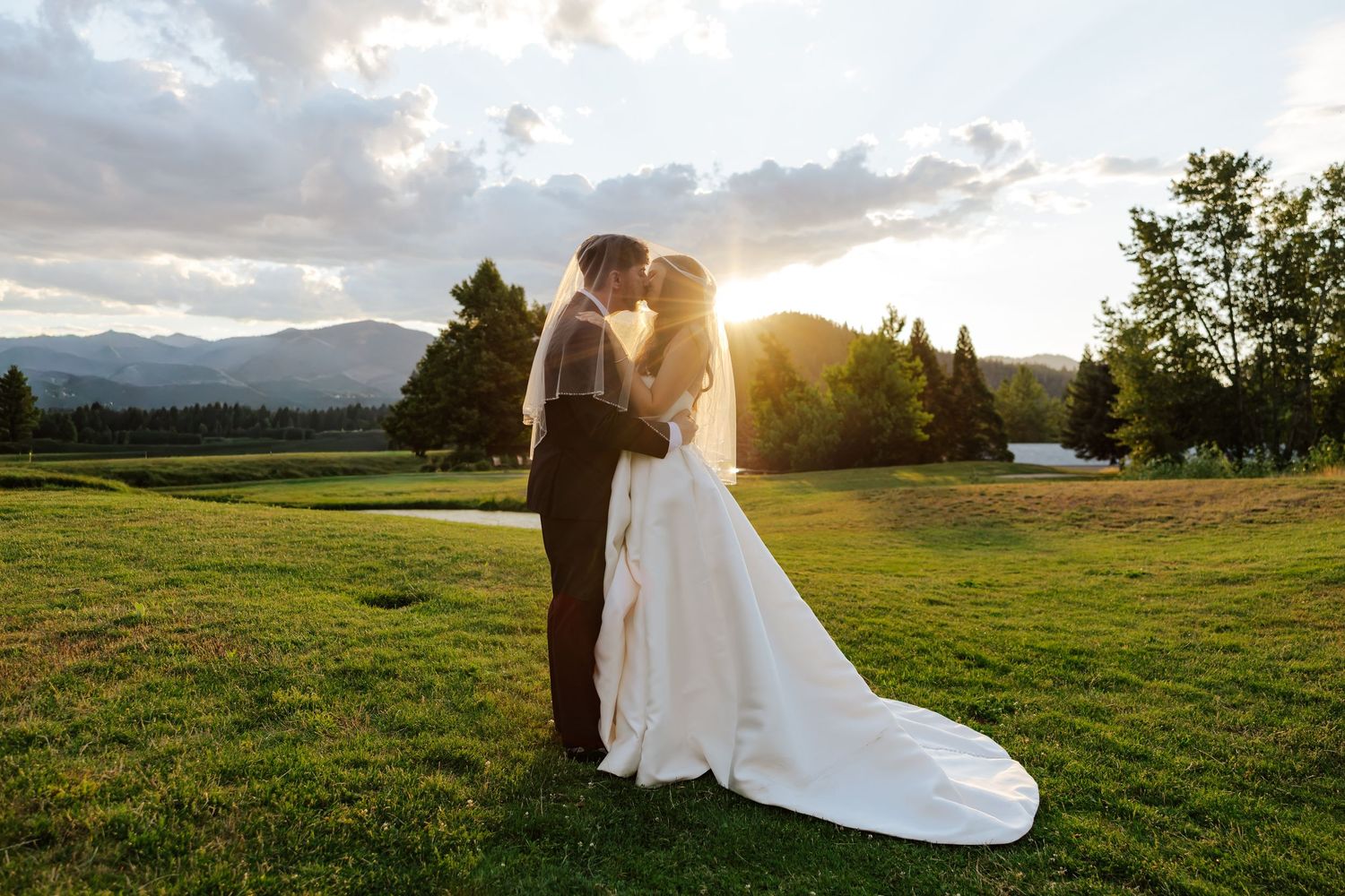 Bride and groom share a sunset kiss on a lush golf course with mountain views.