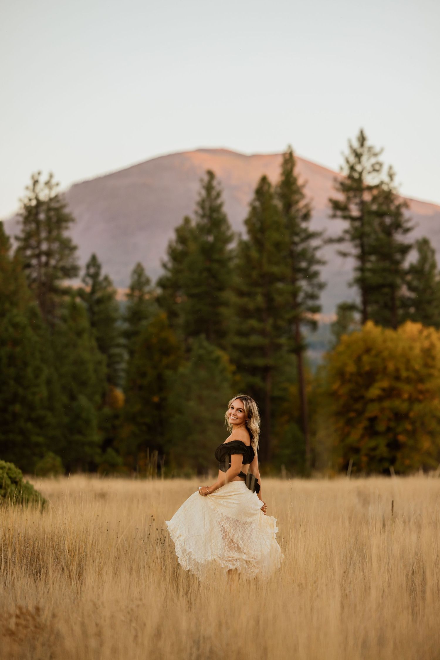 Flowing white dress creates movement against mountain landscape at sunset.