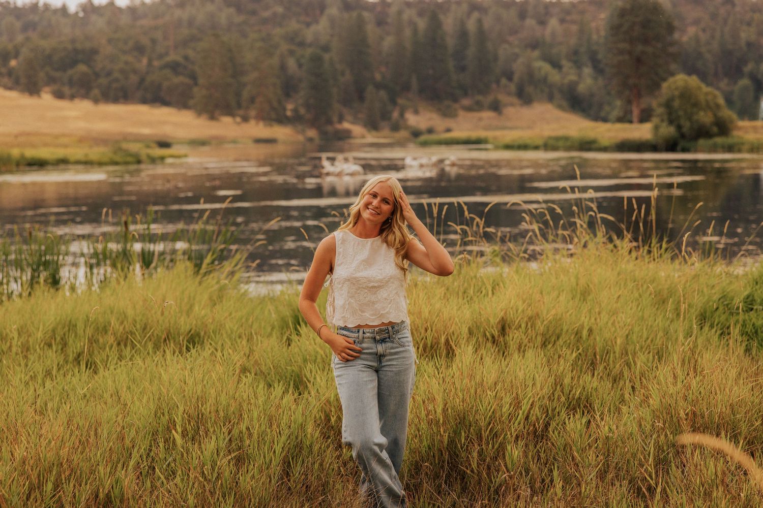 A peaceful lakeside scene with tall grass and mountains in the distance during golden hour.