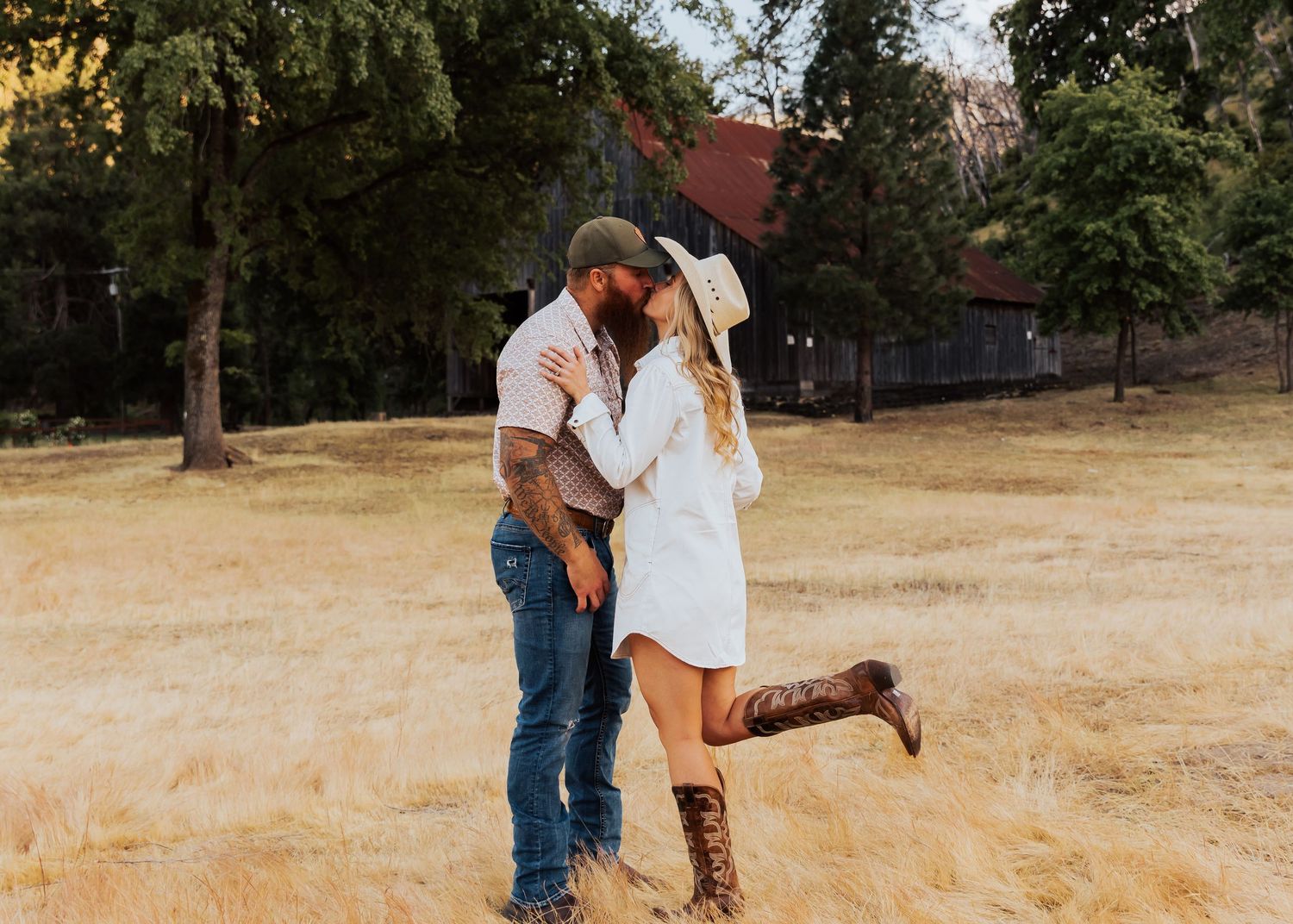 Playful couple dancing and embracing in a golden field near an old barn.