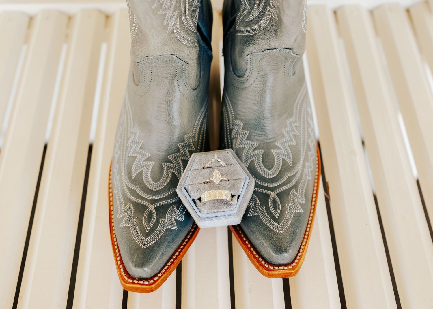 Grey cowboy boots with ornate stitching displayed on white wooden slats.