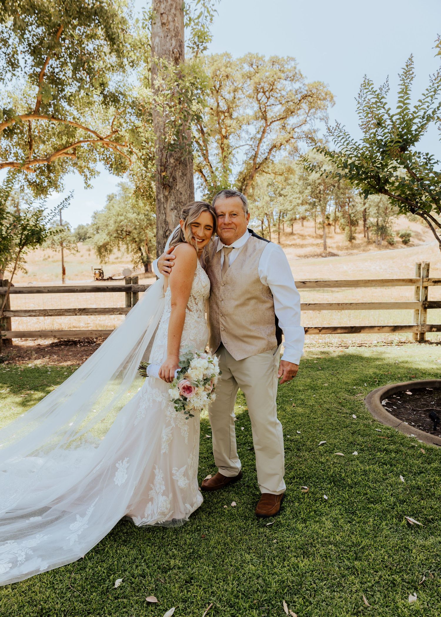 A wedding couple poses in front of a rustic fence with a flowing white dress and bouquet.
