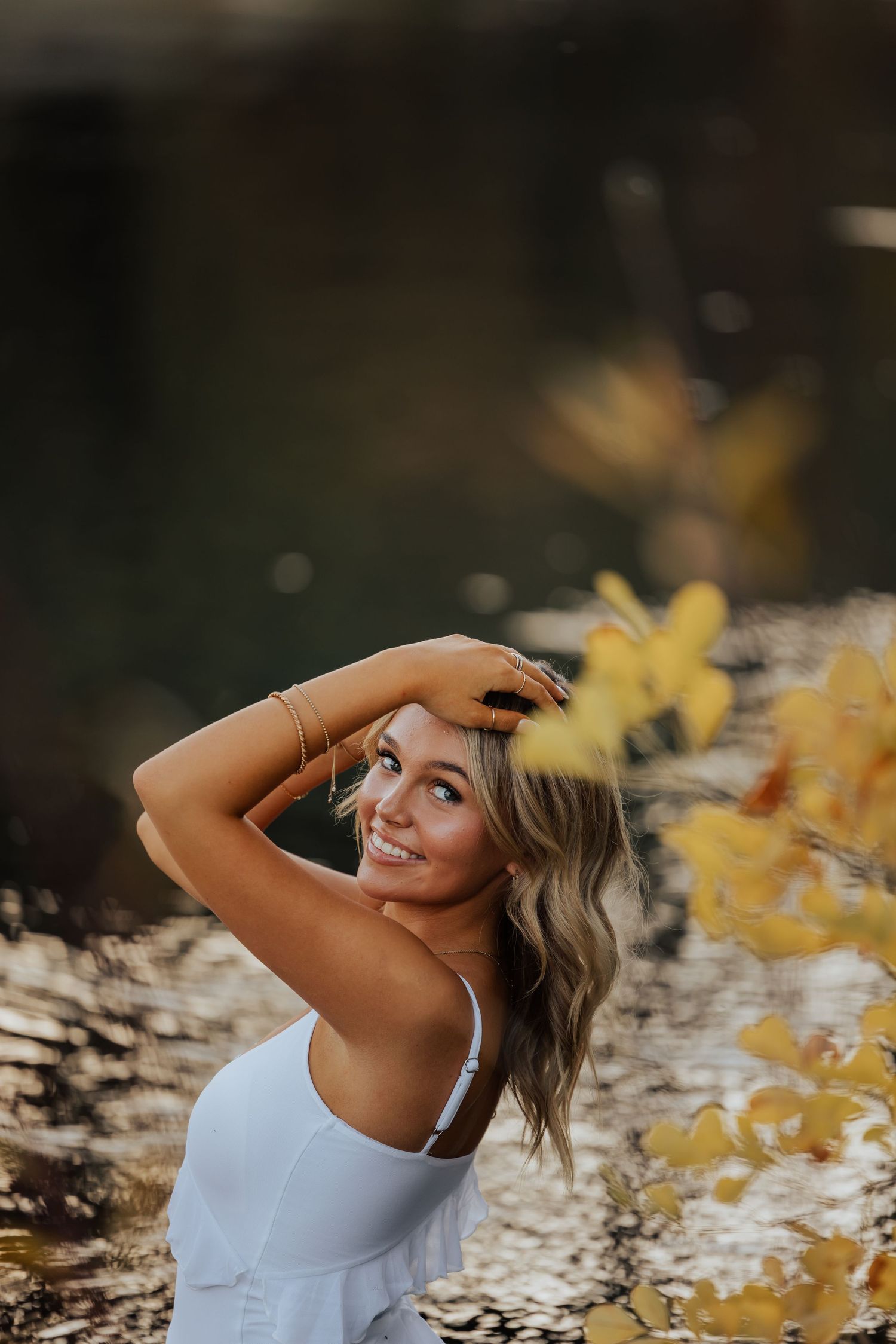 A dreamy autumn photoshoot featuring a white tank top against golden yellow leaves in soft lighting.
