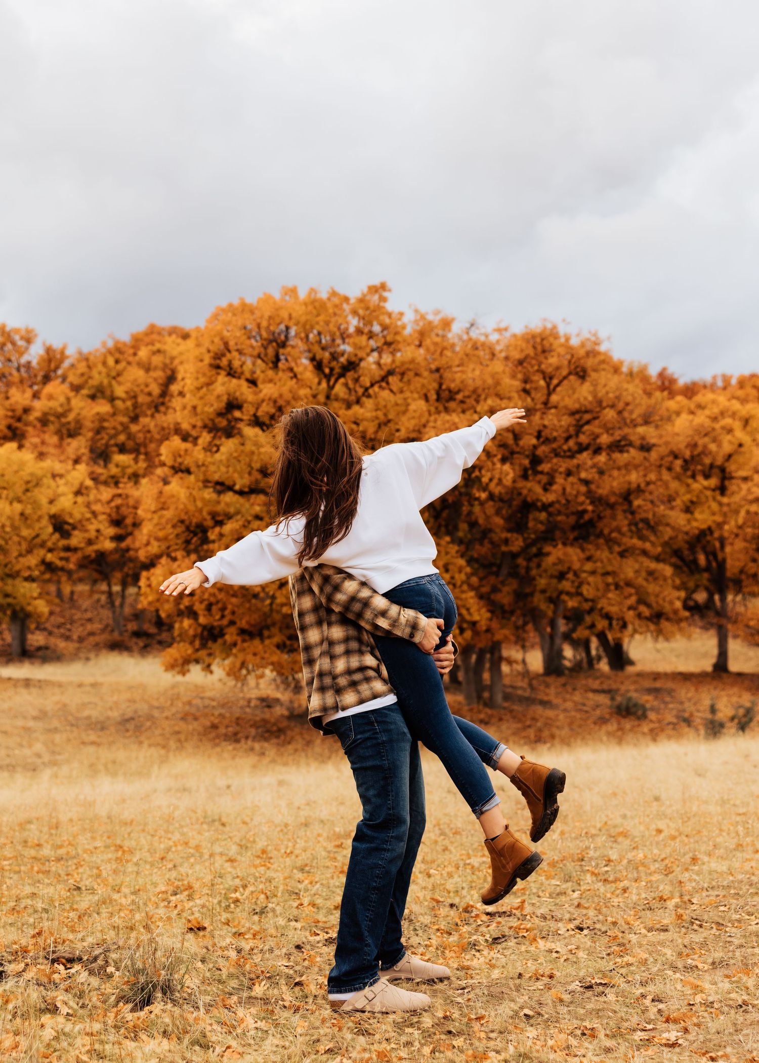 Couple sharing a joyful spinning moment in a golden autumn field.