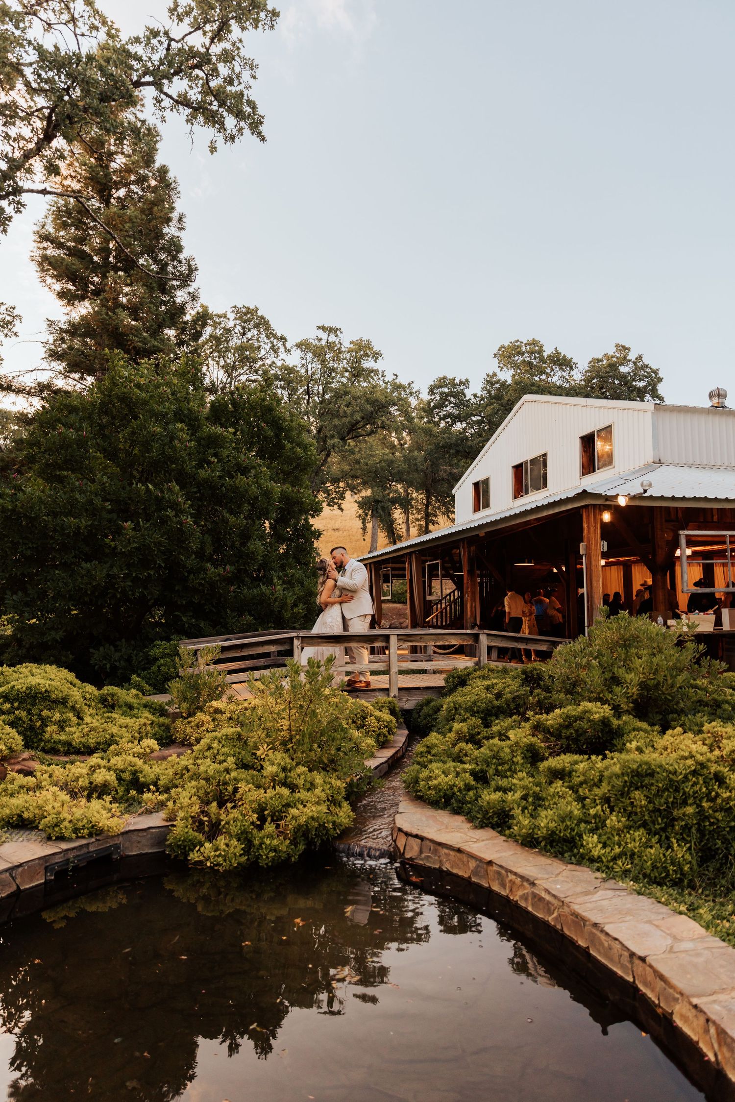 A rustic wooden walkway leads to waterfront cabins surrounded by lush greenery.