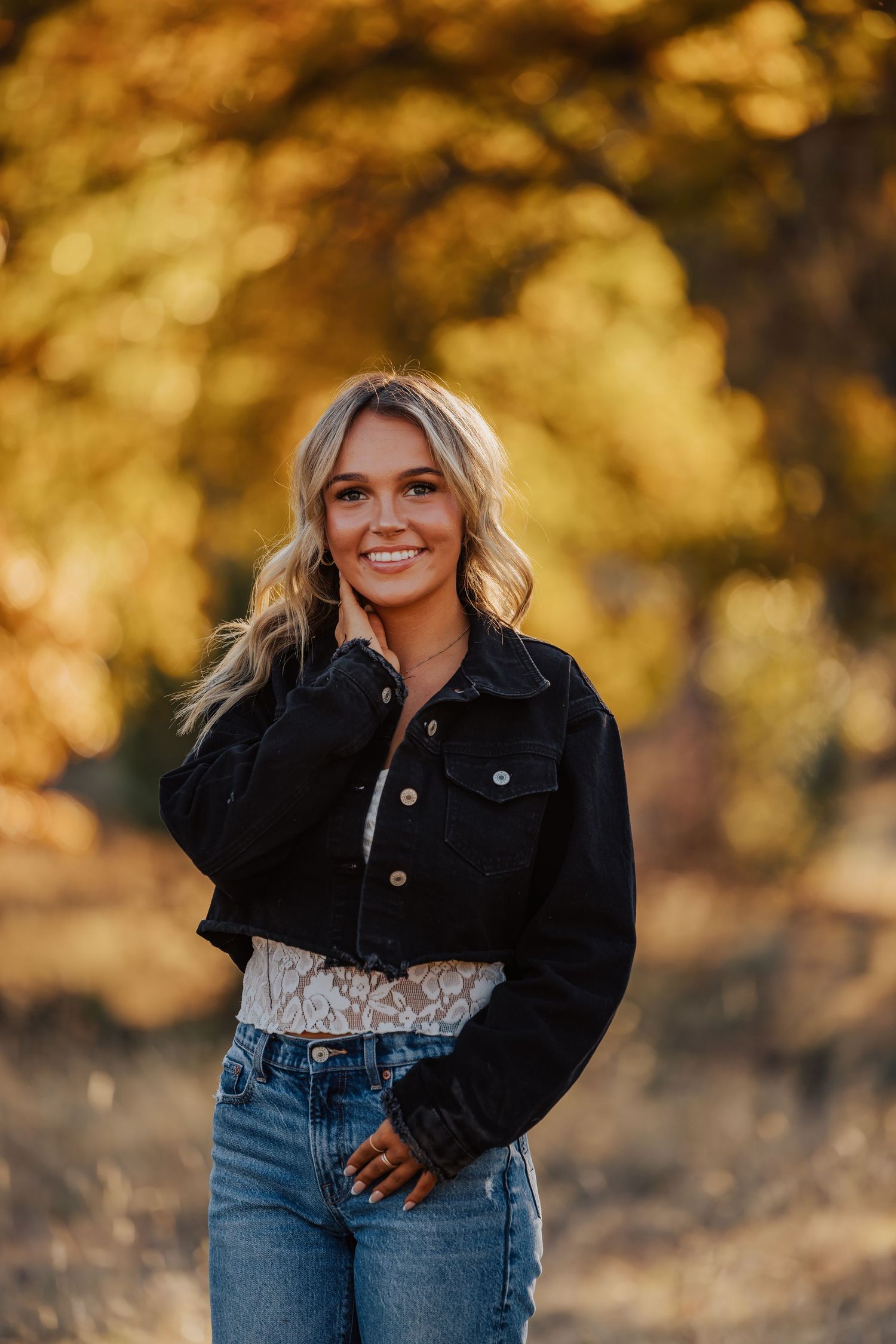 Casual outdoor portrait with denim and black jacket against autumn scenery.