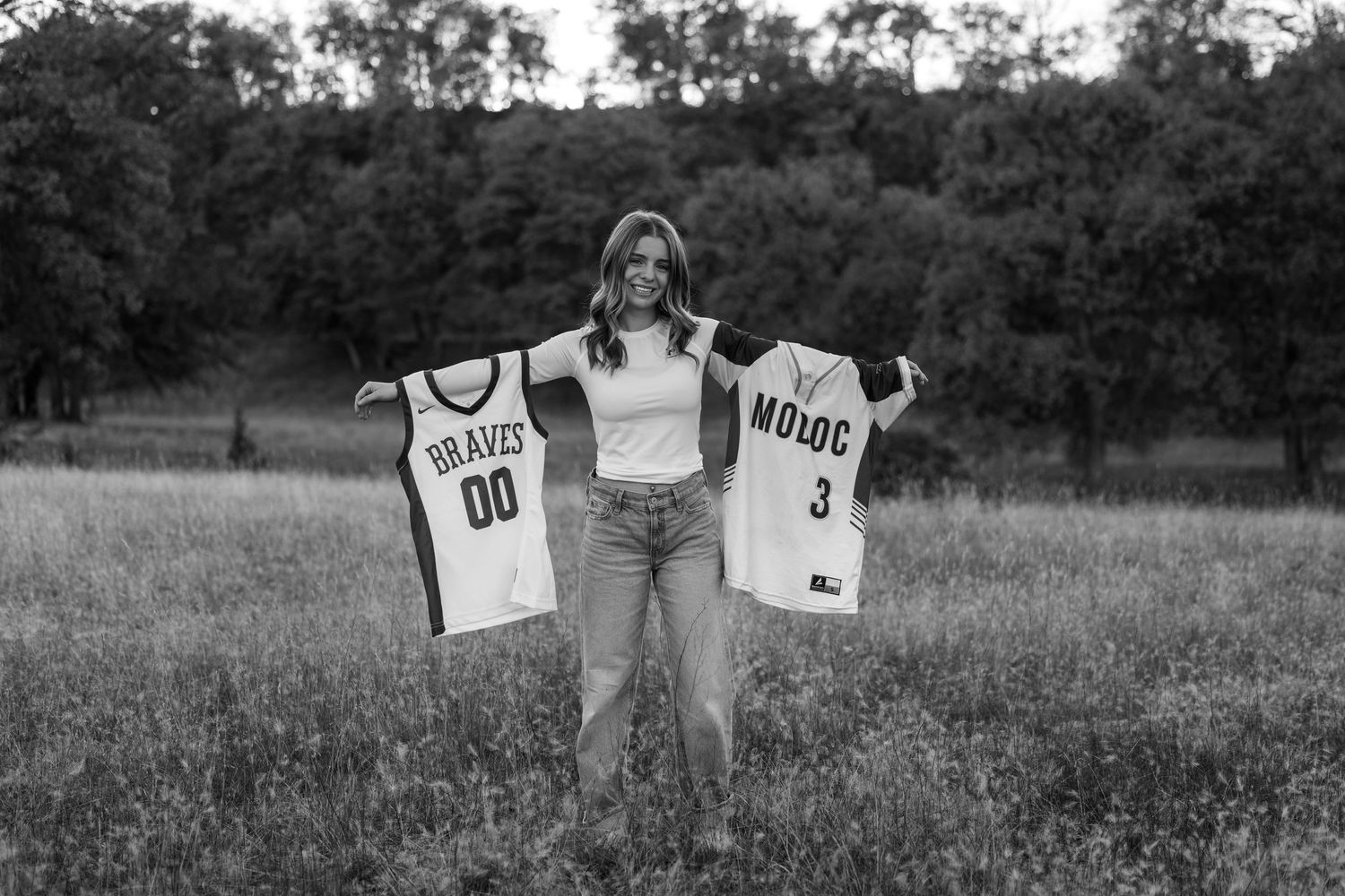Someone holding up sports jerseys in a grassy field during a photoshoot.