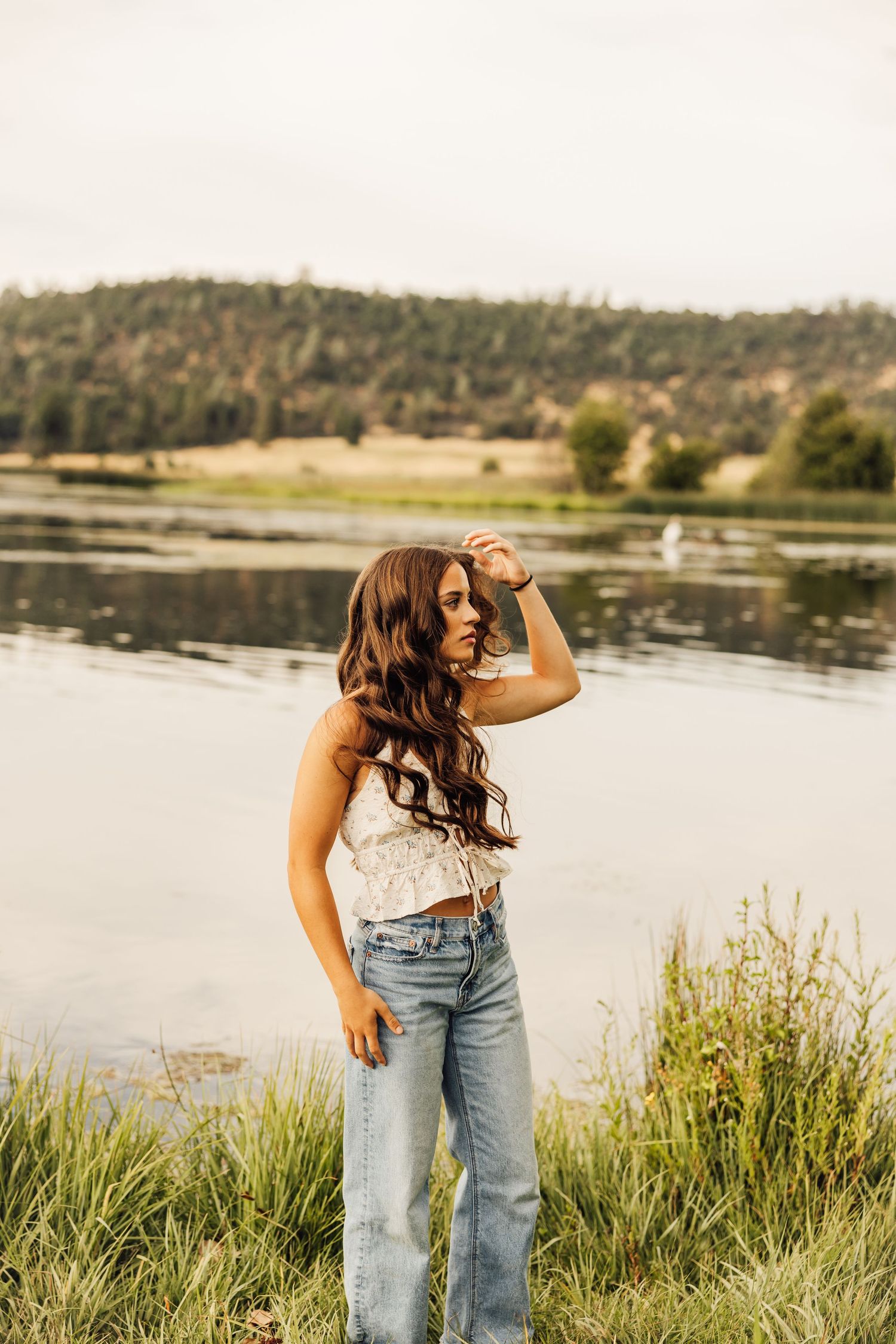 Summer photoshoot by a tranquil lake with natural grass and mountain scenery.