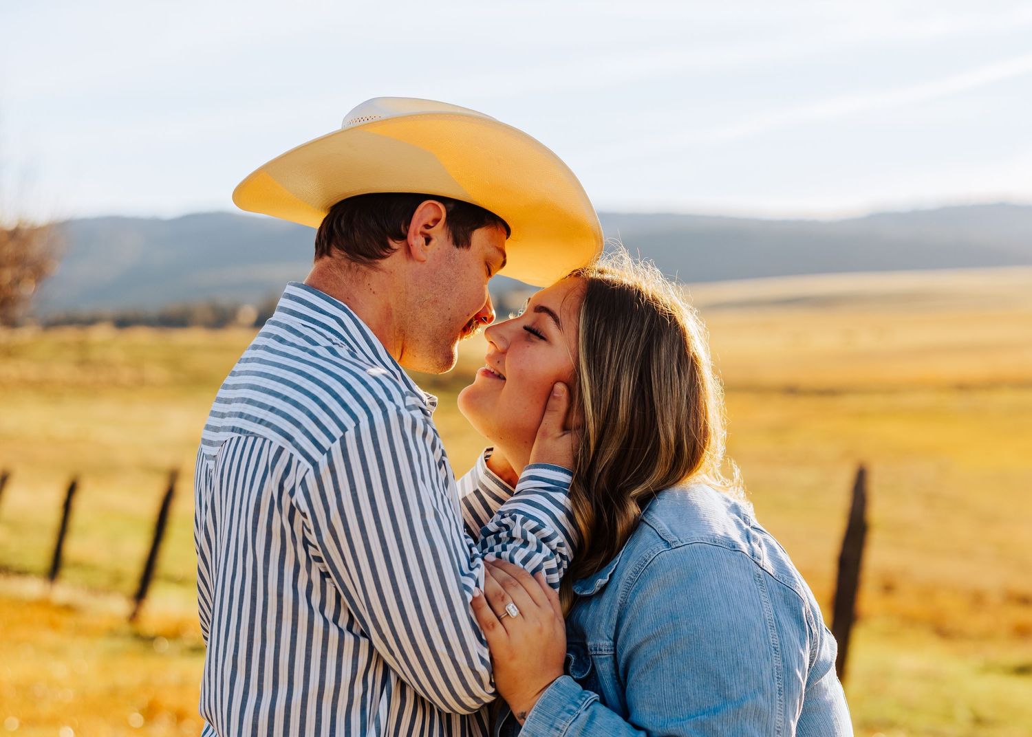 A romantic engagement photoshoot in a golden field with mountains in the background.