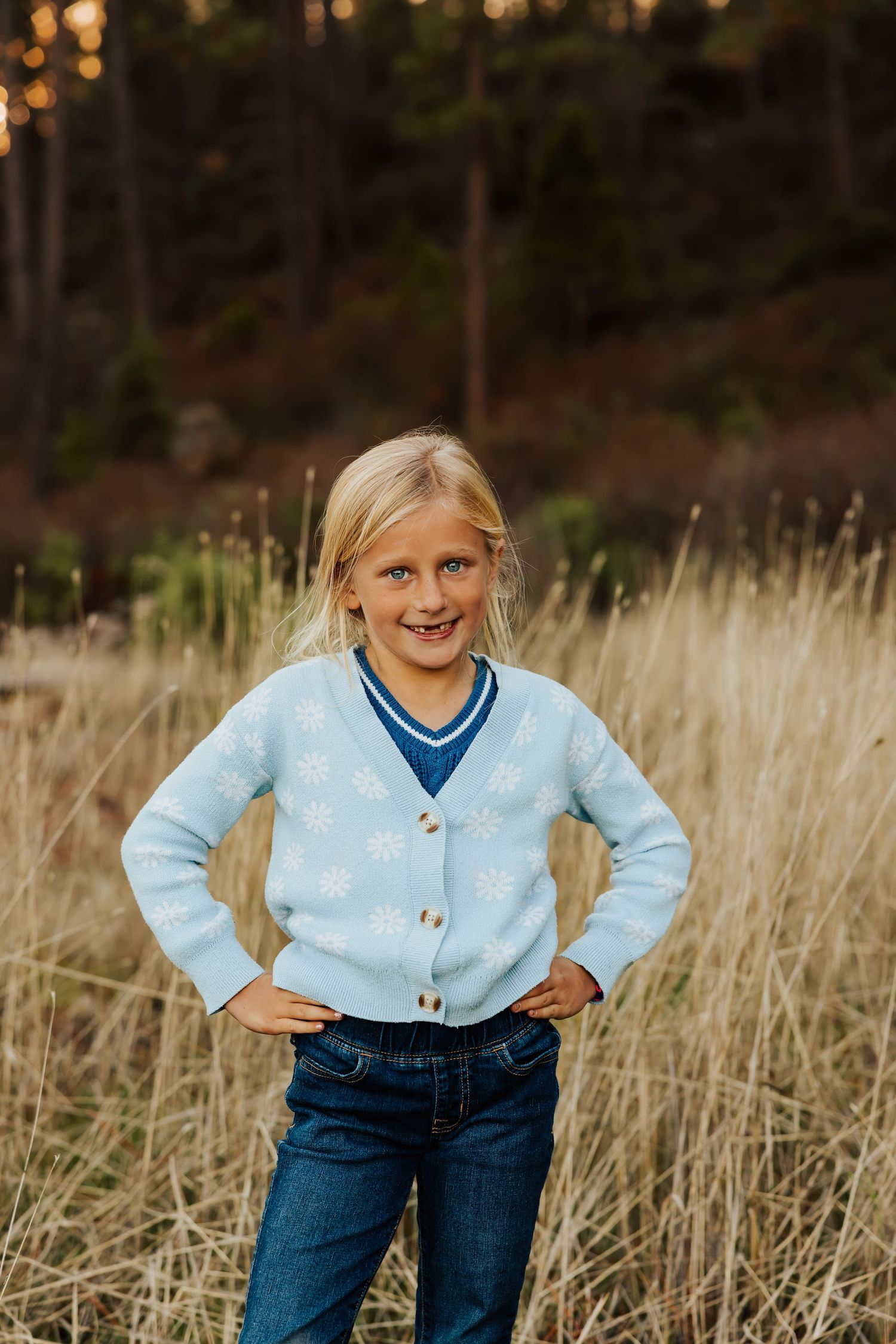 Young person in light blue cardigan and jeans poses playfully in golden field.