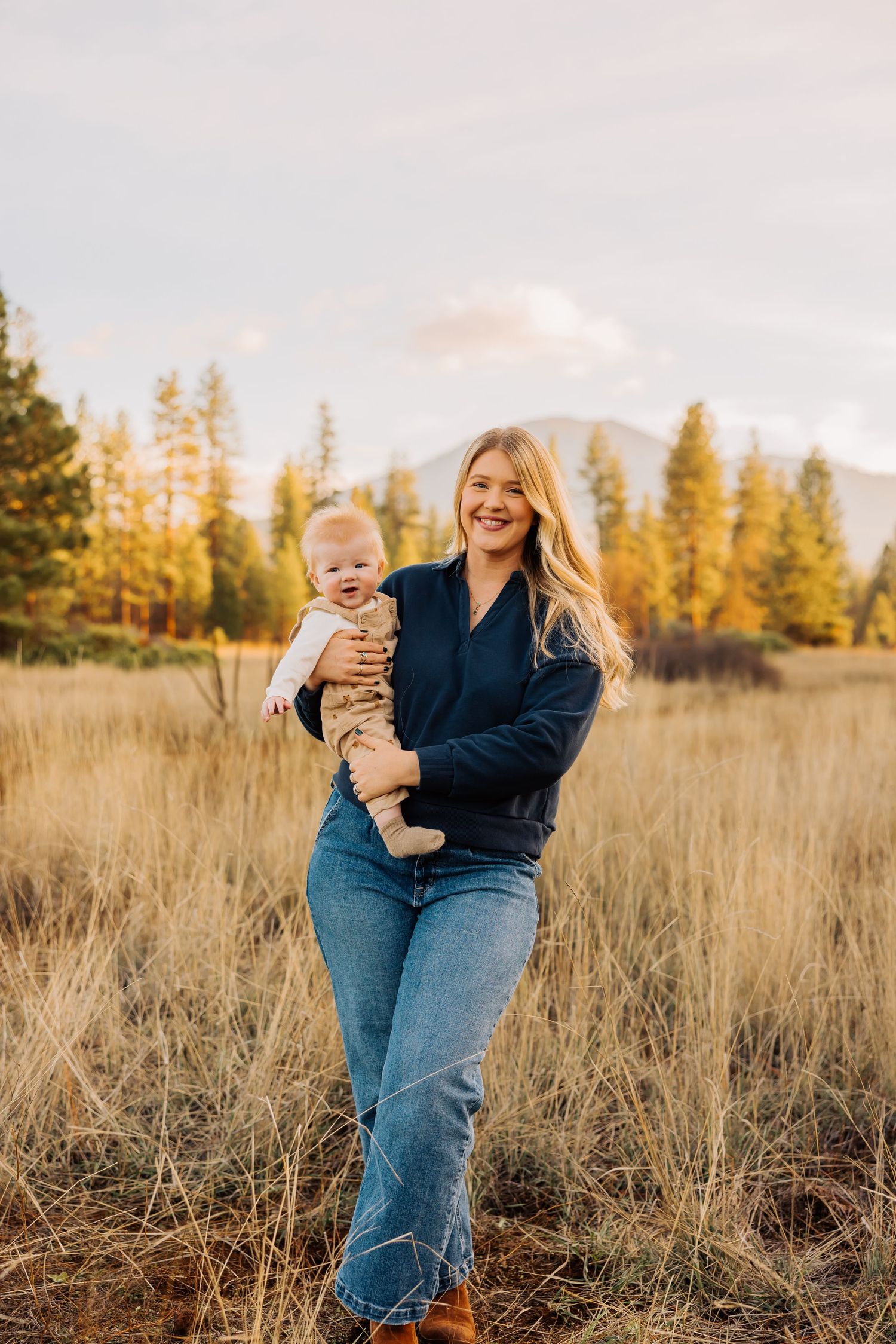 A mother and baby share a moment in an autumn field with mountains in the background.