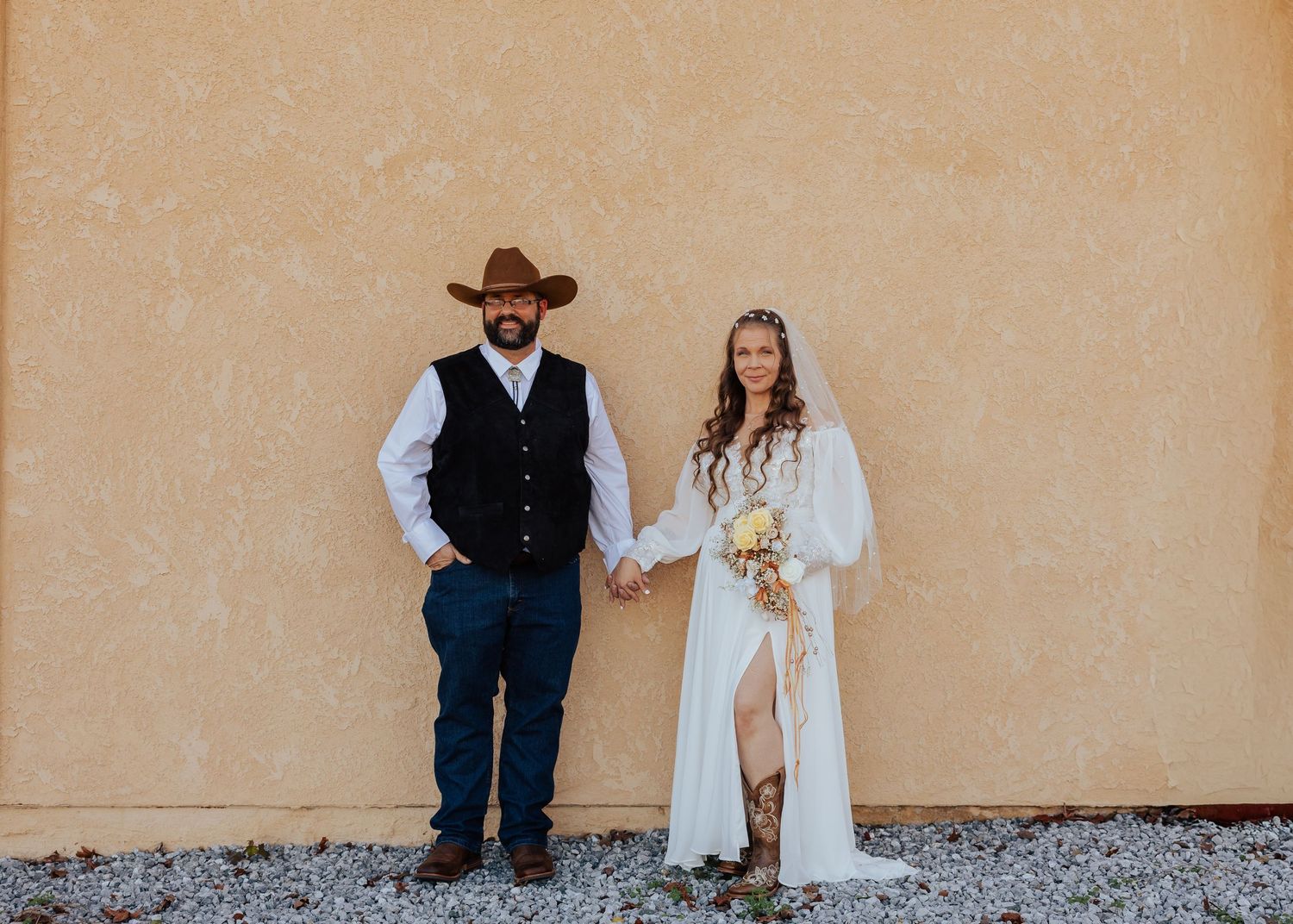 Rustic wedding portrait against a terracotta wall showcasing western-inspired attire.