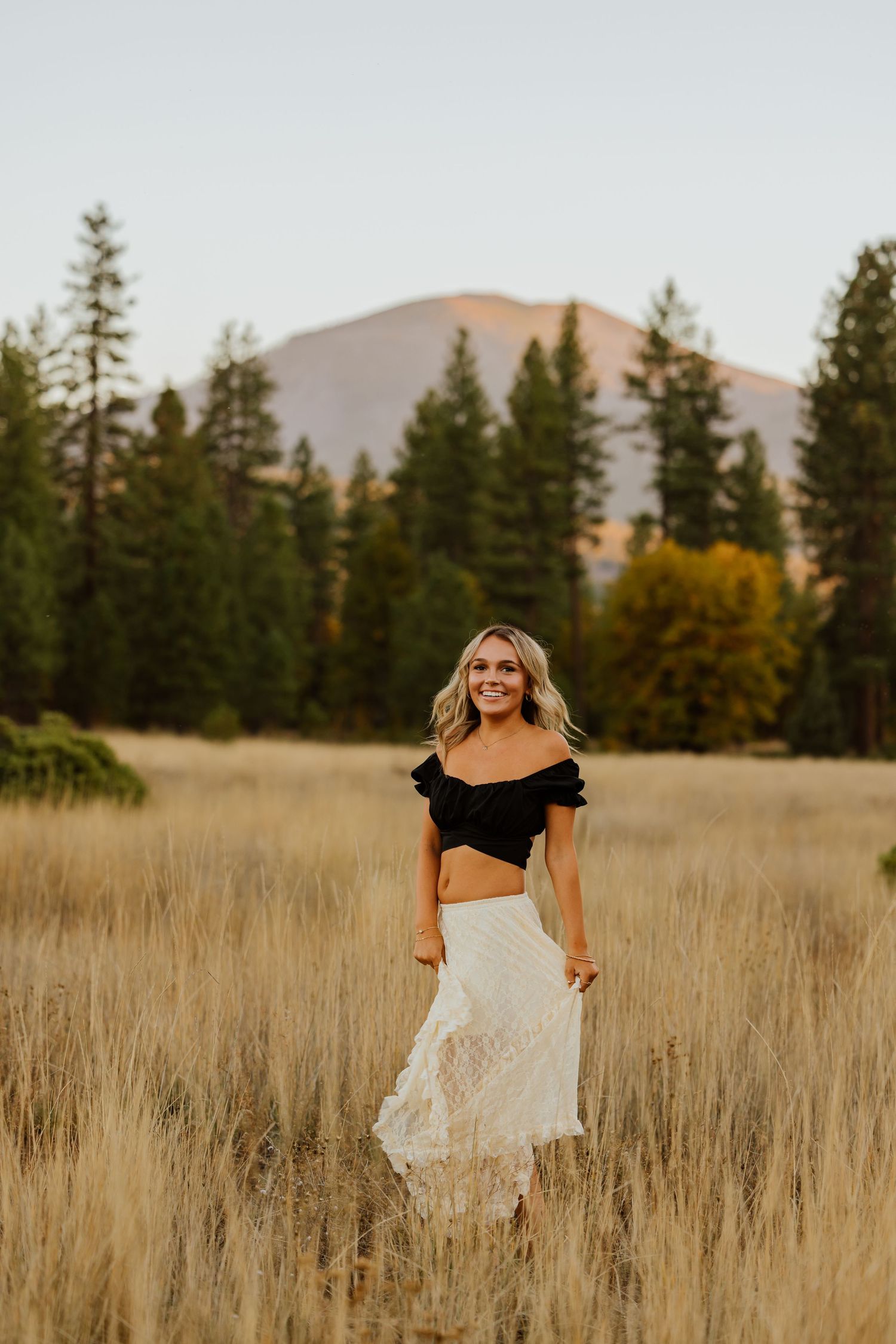 Dancing in a wheat field wearing a white skirt and black top with mountains in the distance.