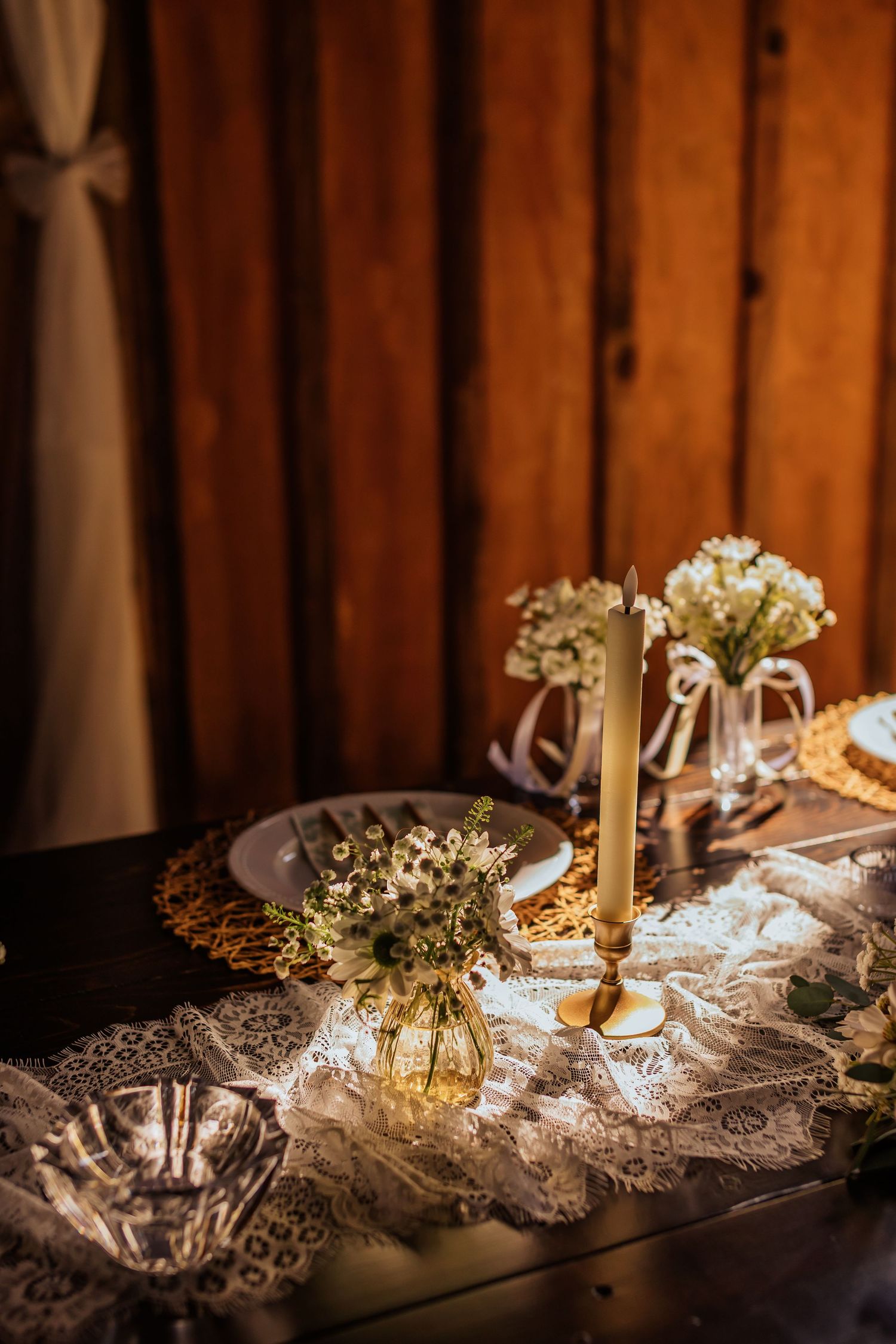 Elegant table setting with lace, candles and baby's breath flowers against dark wood background.