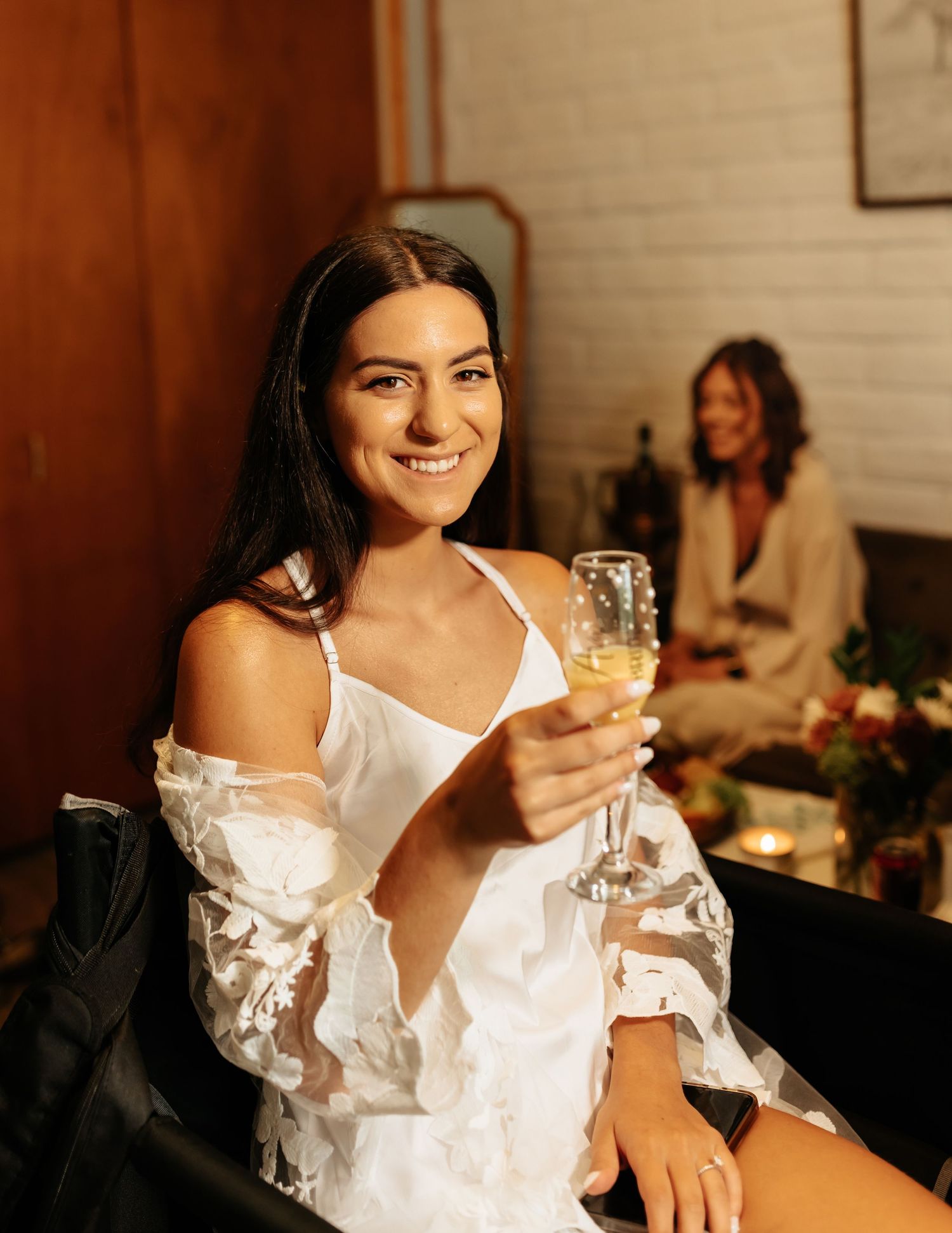 Woman in white dress smiling while holding champagne glass at wedding reception.