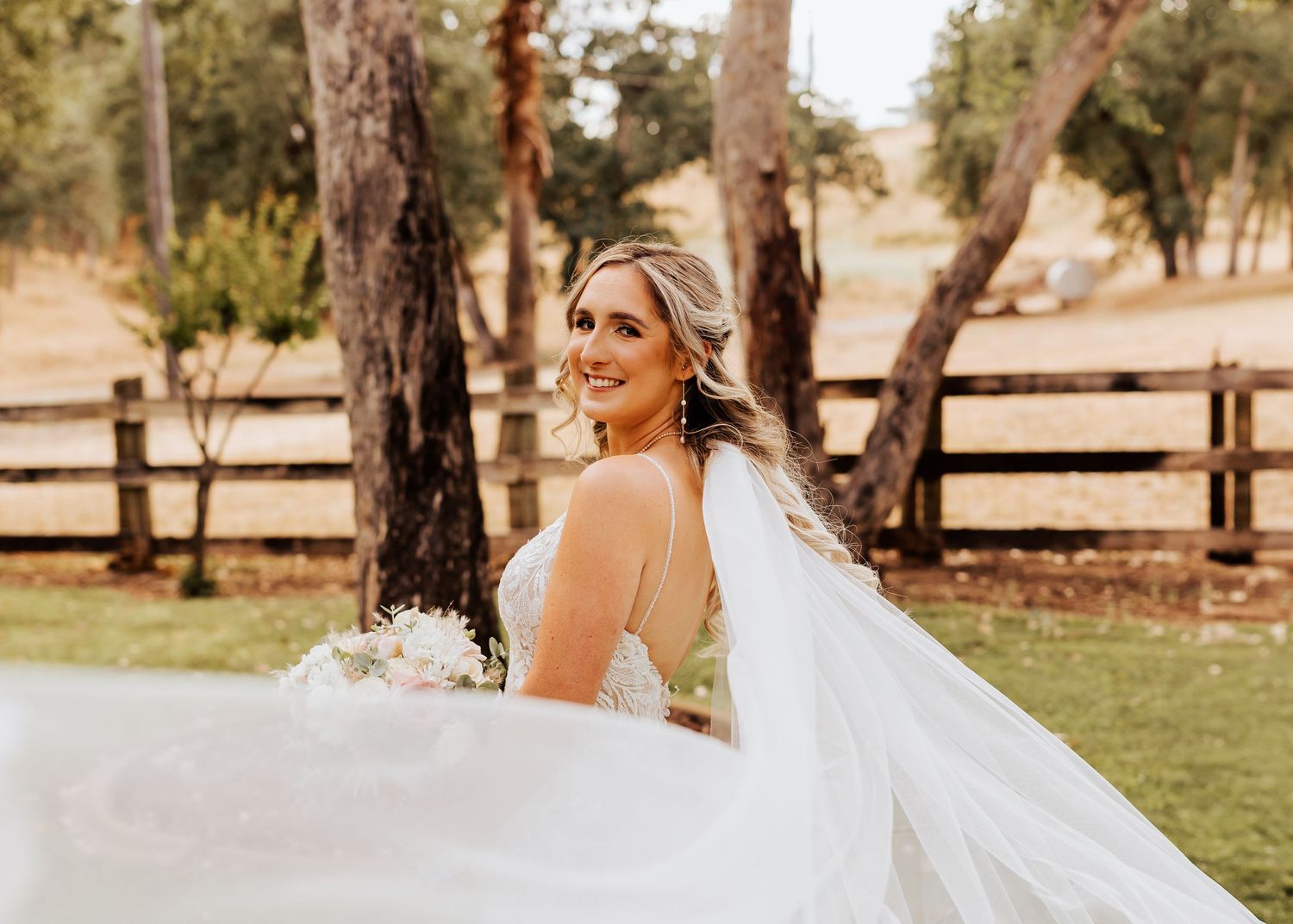 Flowing white wedding dress and veil captured in motion against a rustic ranch backdrop.
