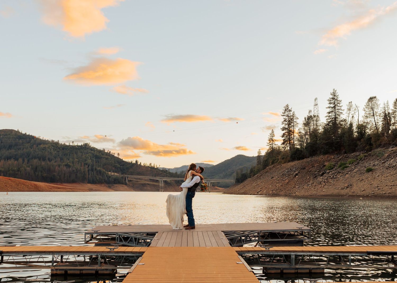 Romantic lakeside dock photos at sunset with mountain backdrop and calm waters.