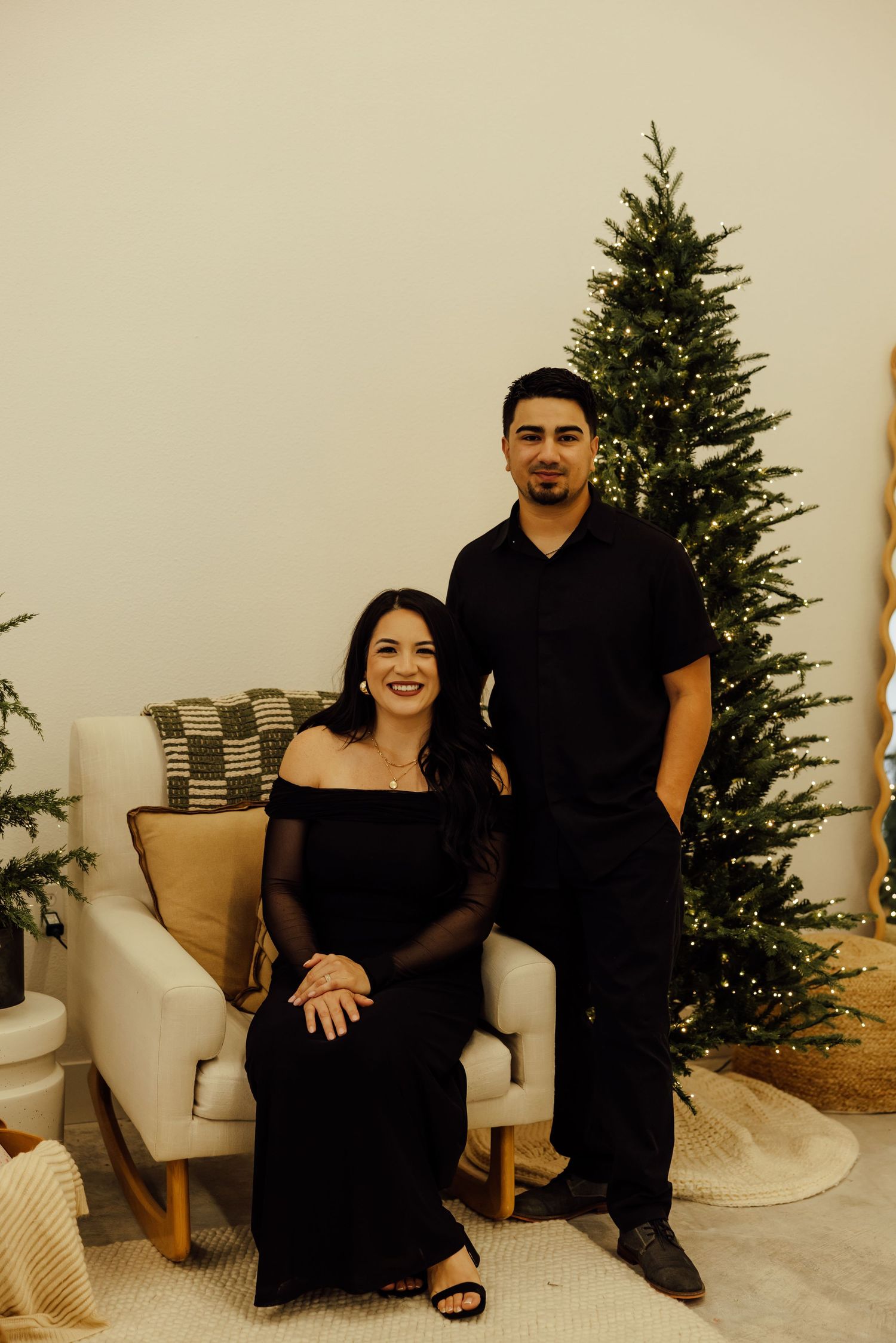A group in coordinated black outfits poses together on a white couch near a Christmas tree.