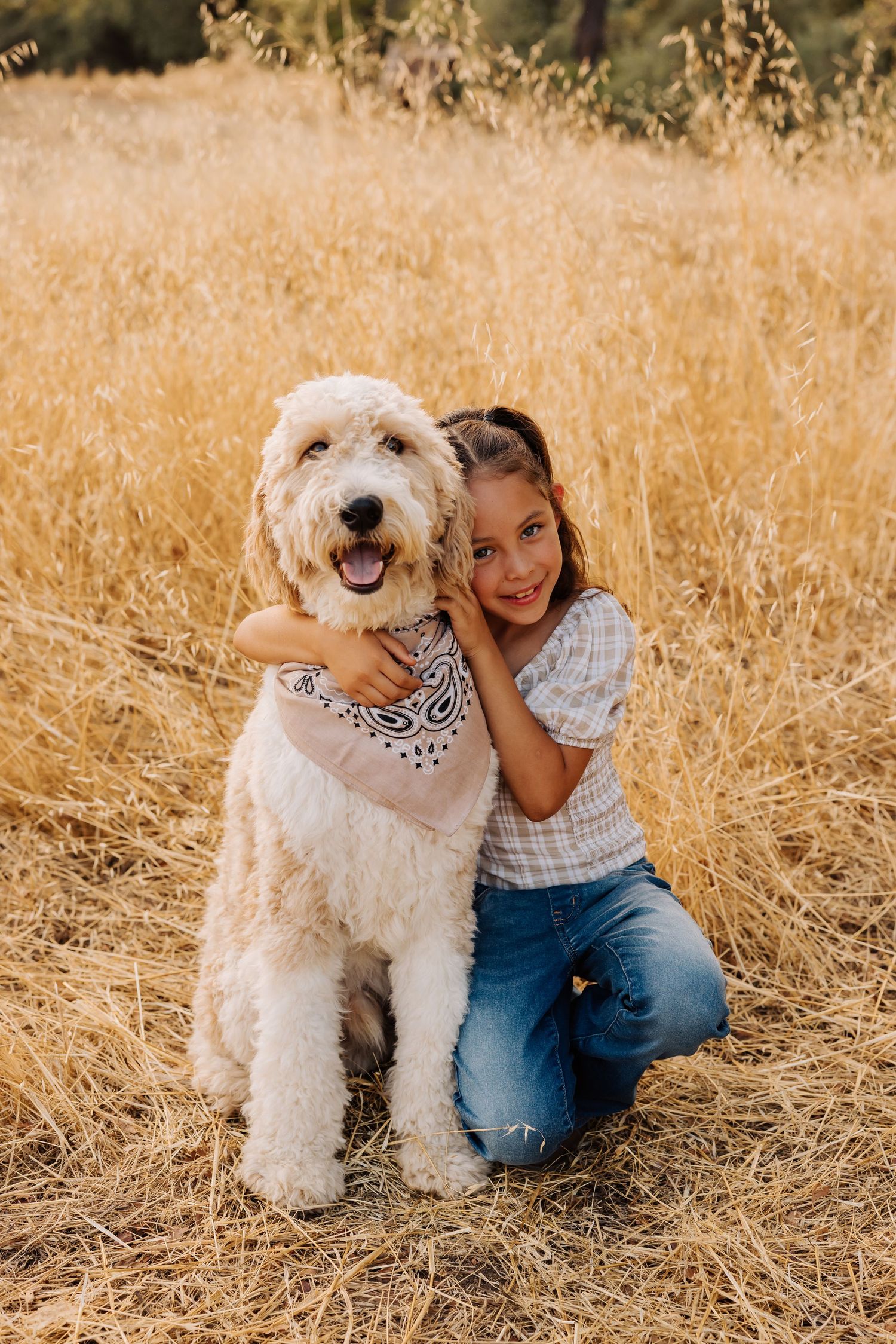 White fluffy dog and children pose together in sunlit field.