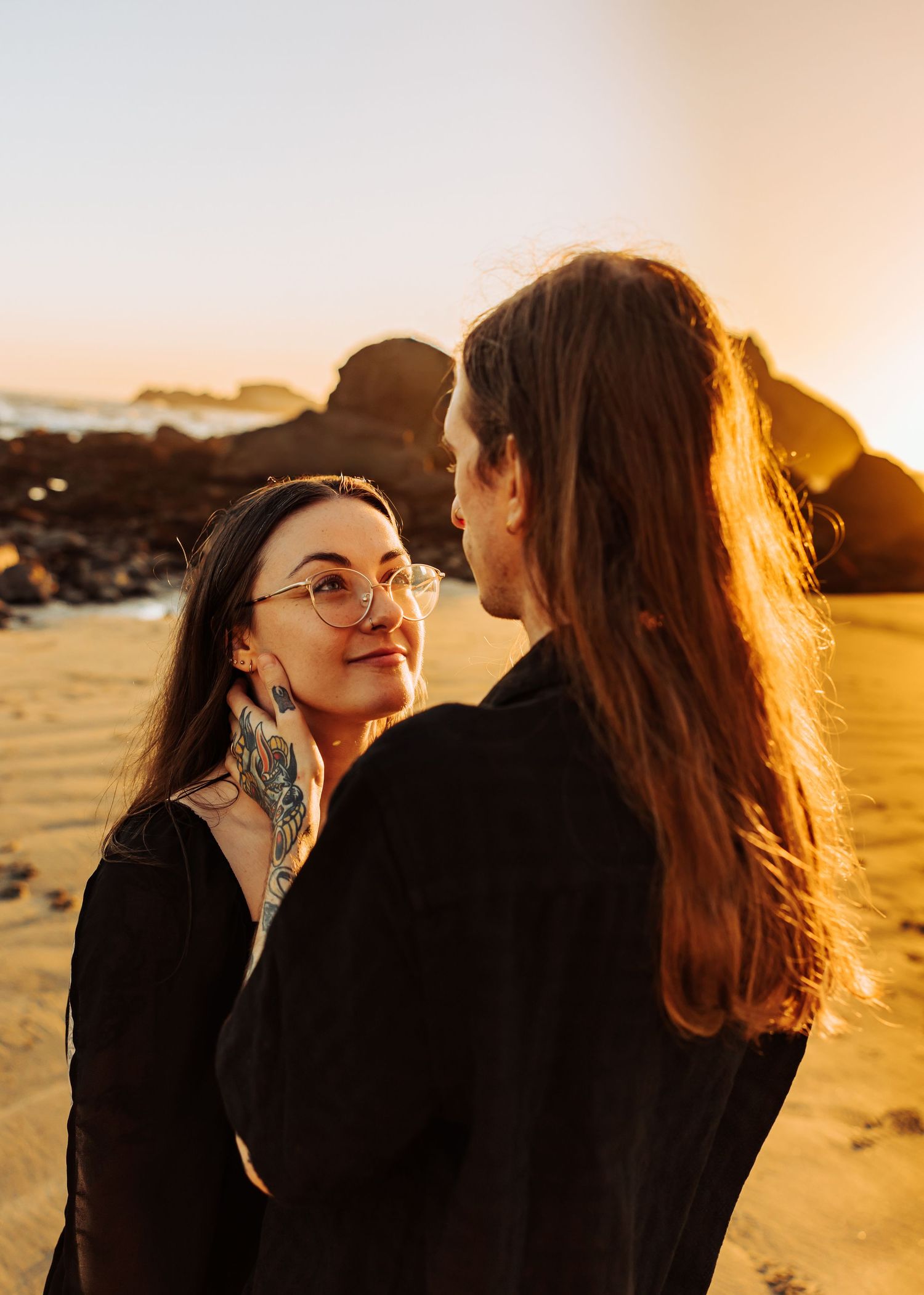 Intimate couple moment on beach at sunset with golden light and coastal rocks.