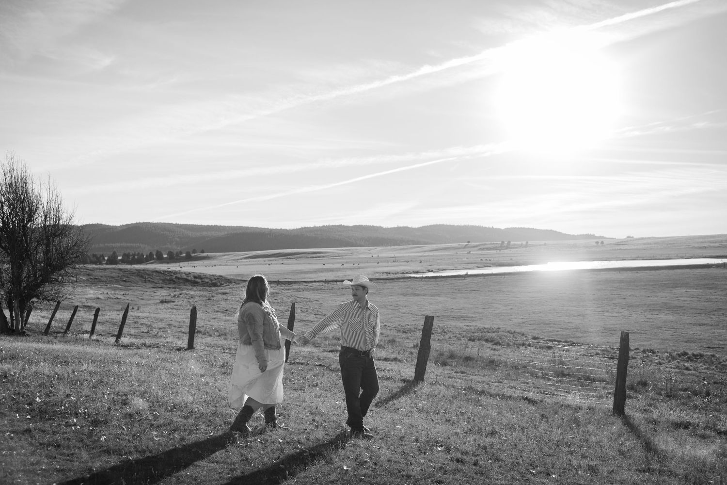 A couple walking hand in hand across an open field during sunset.