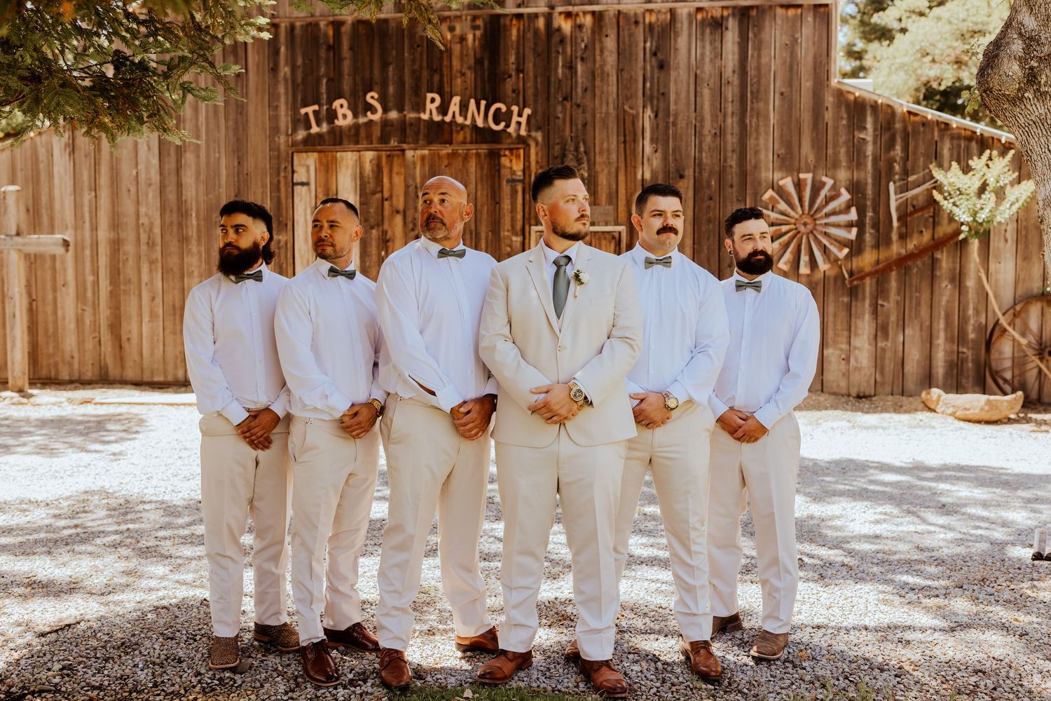 Wedding party members lined up in white and cream formal attire against rustic barn backdrop.