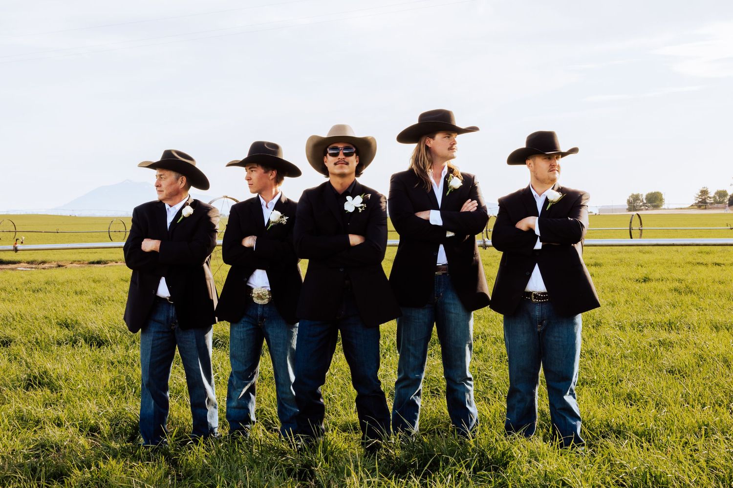 Groomsmen in cowboy hats and jeans pose together in a grassy field.