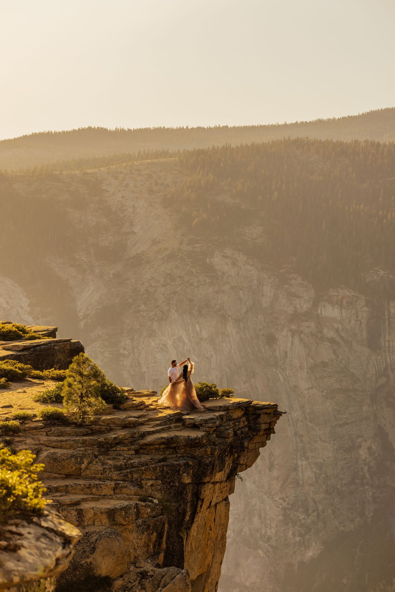 Two horses stand silhouetted against a sunset sky on a dramatic rocky cliff edge at Yosemite National Park.
