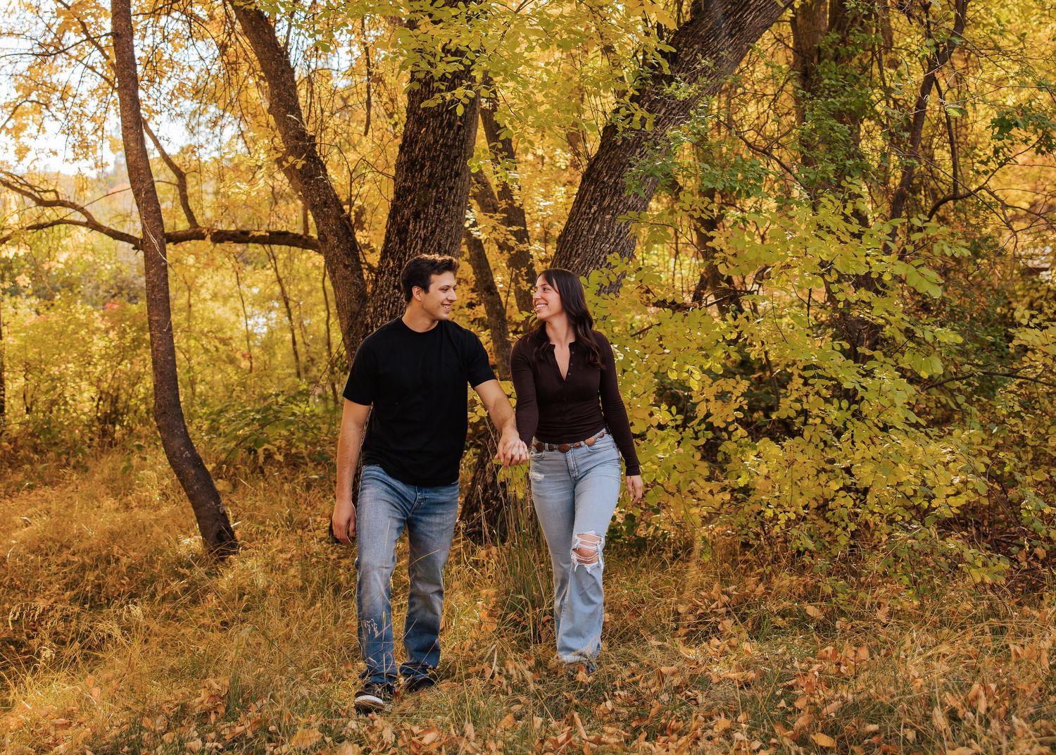 A couple walking through golden autumn trees during a fall photoshoot.