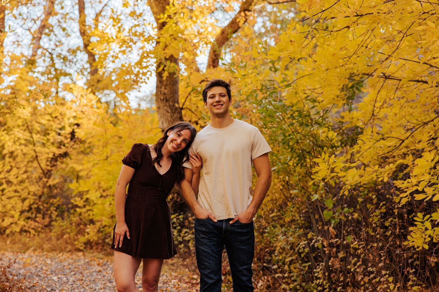 Couple walking hand in hand through yellow fall foliage.
