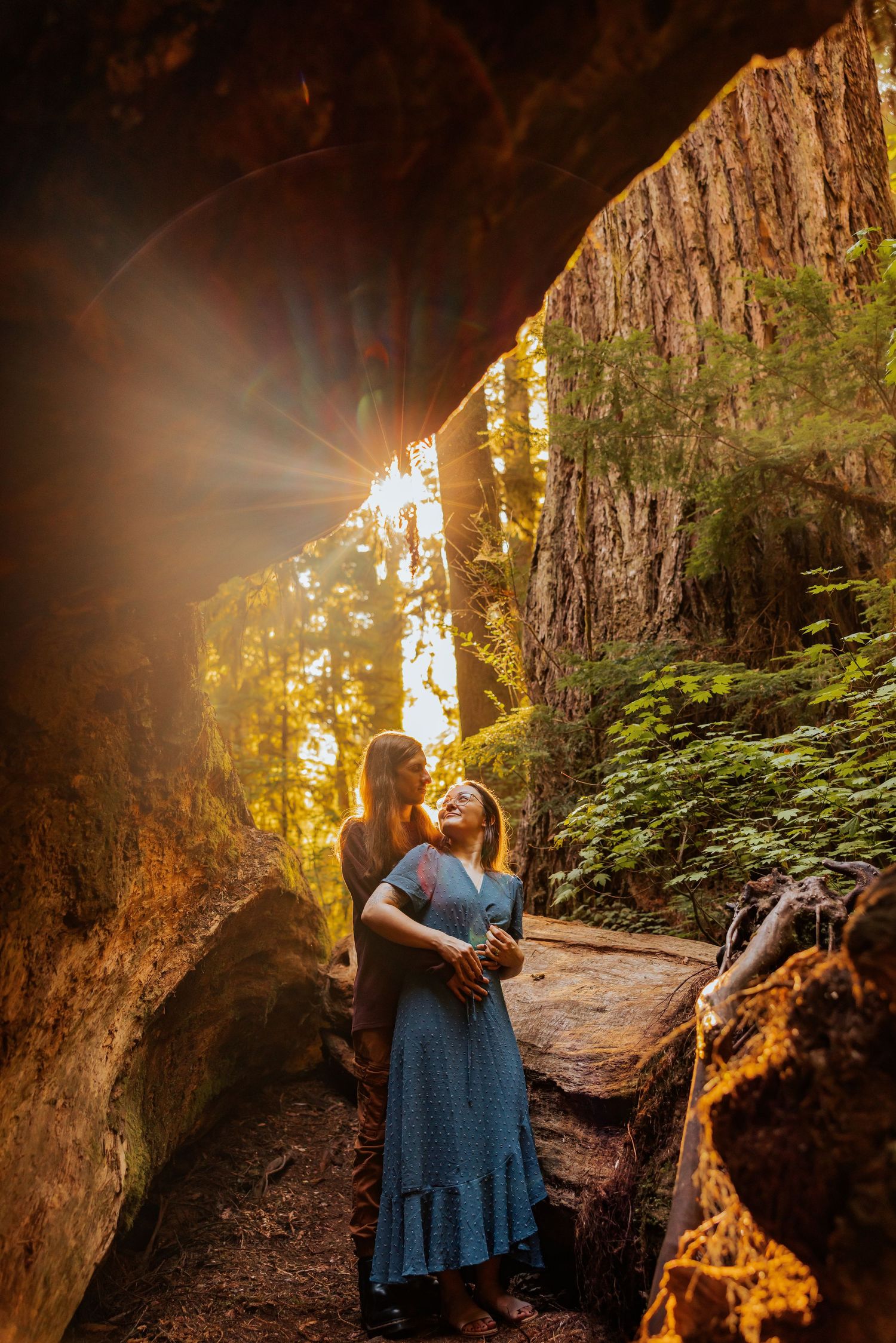 A romantic moment captured in a cave opening with sunbeams streaming through the forest.