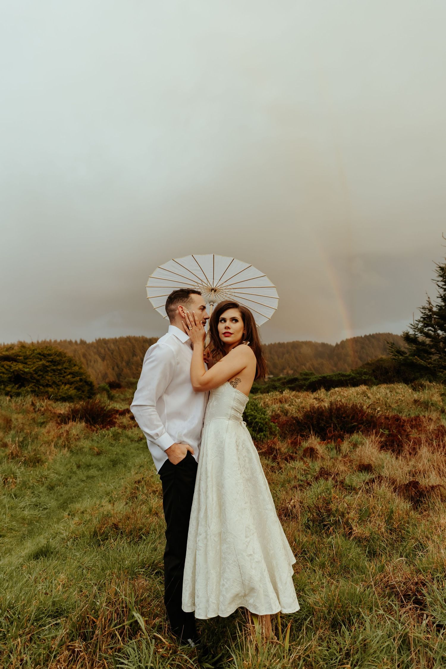 A romantic couple shares intimate moments on a misty coastal hillside with a white parasol.
