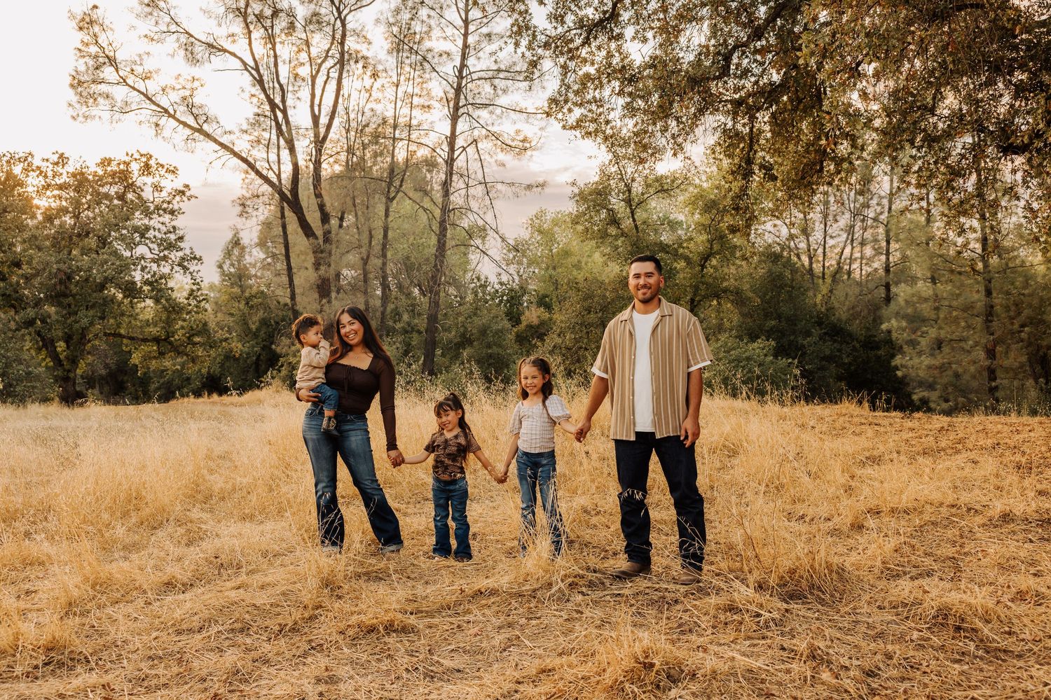 Family walking together through tall grass field during golden hour photography session.