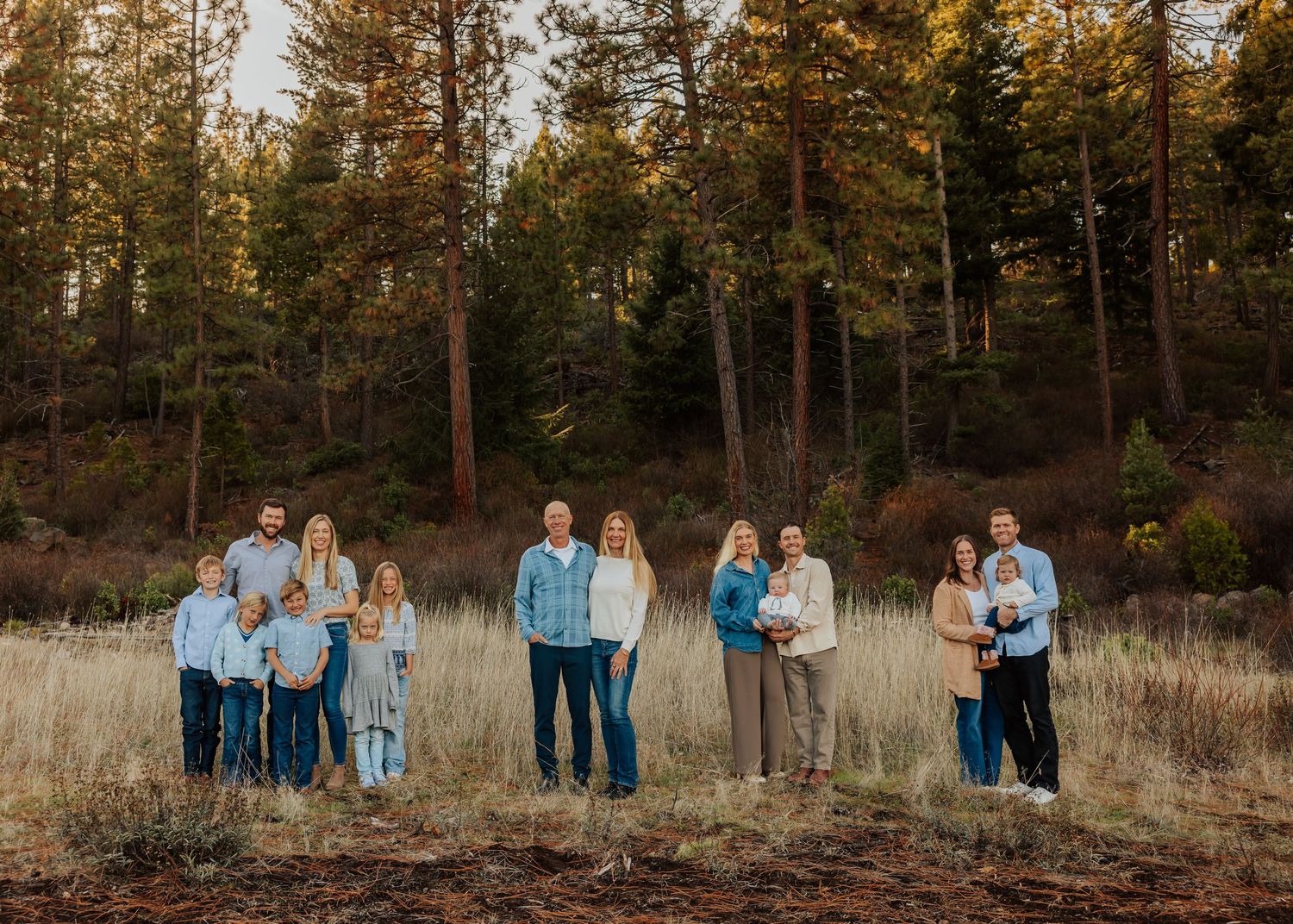 Family photo series in autumn field with tall grass and pine trees.