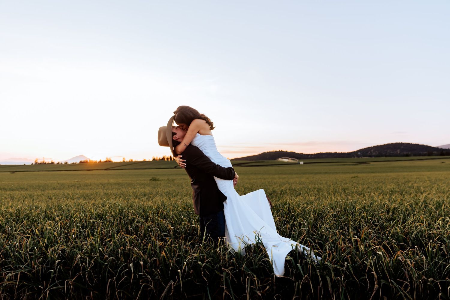Dramatic silhouette of newlyweds against a vast rural landscape at sunset.
