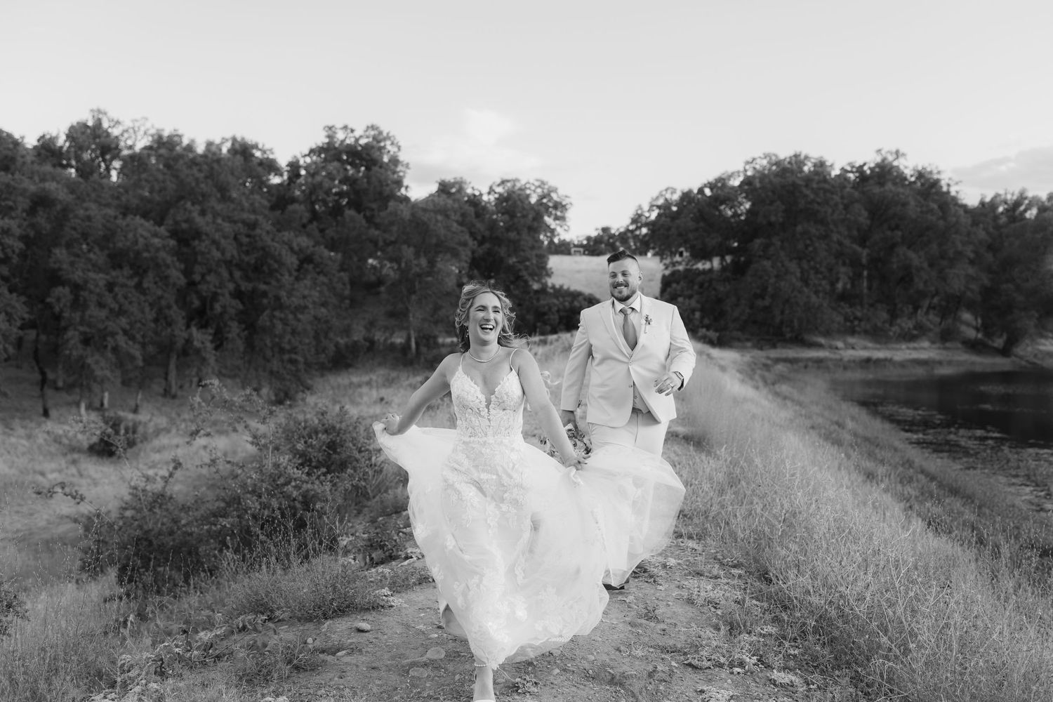 A joyful couple running along a countryside path in wedding attire.