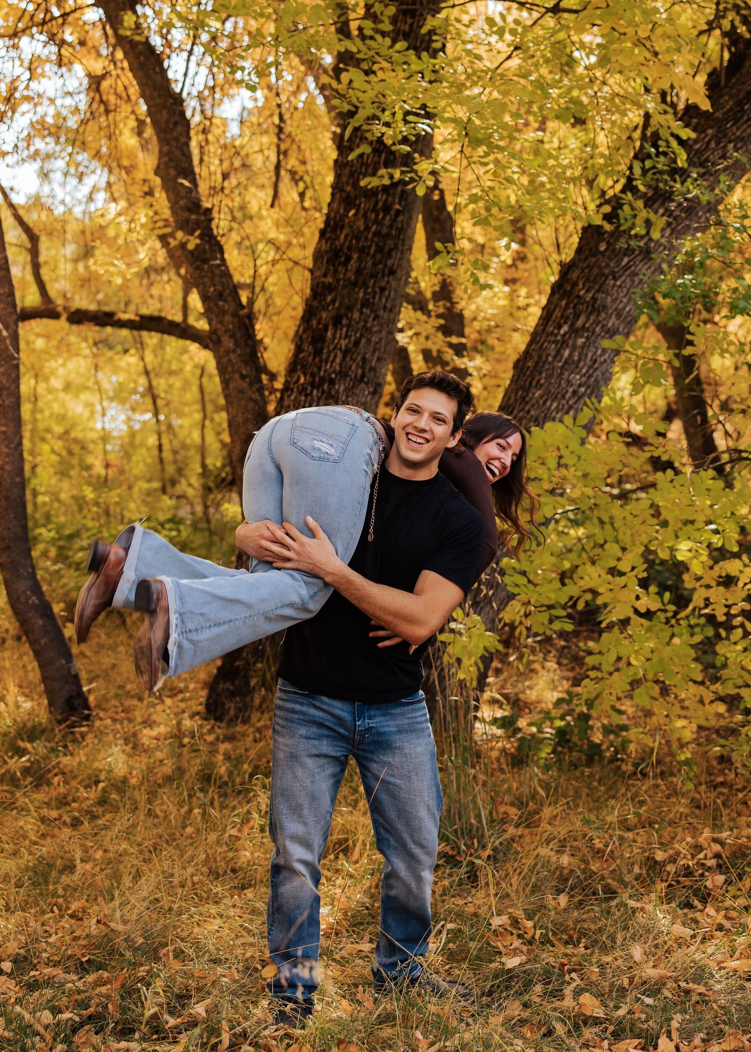Playful couple poses among fall foliage in a wooded setting.