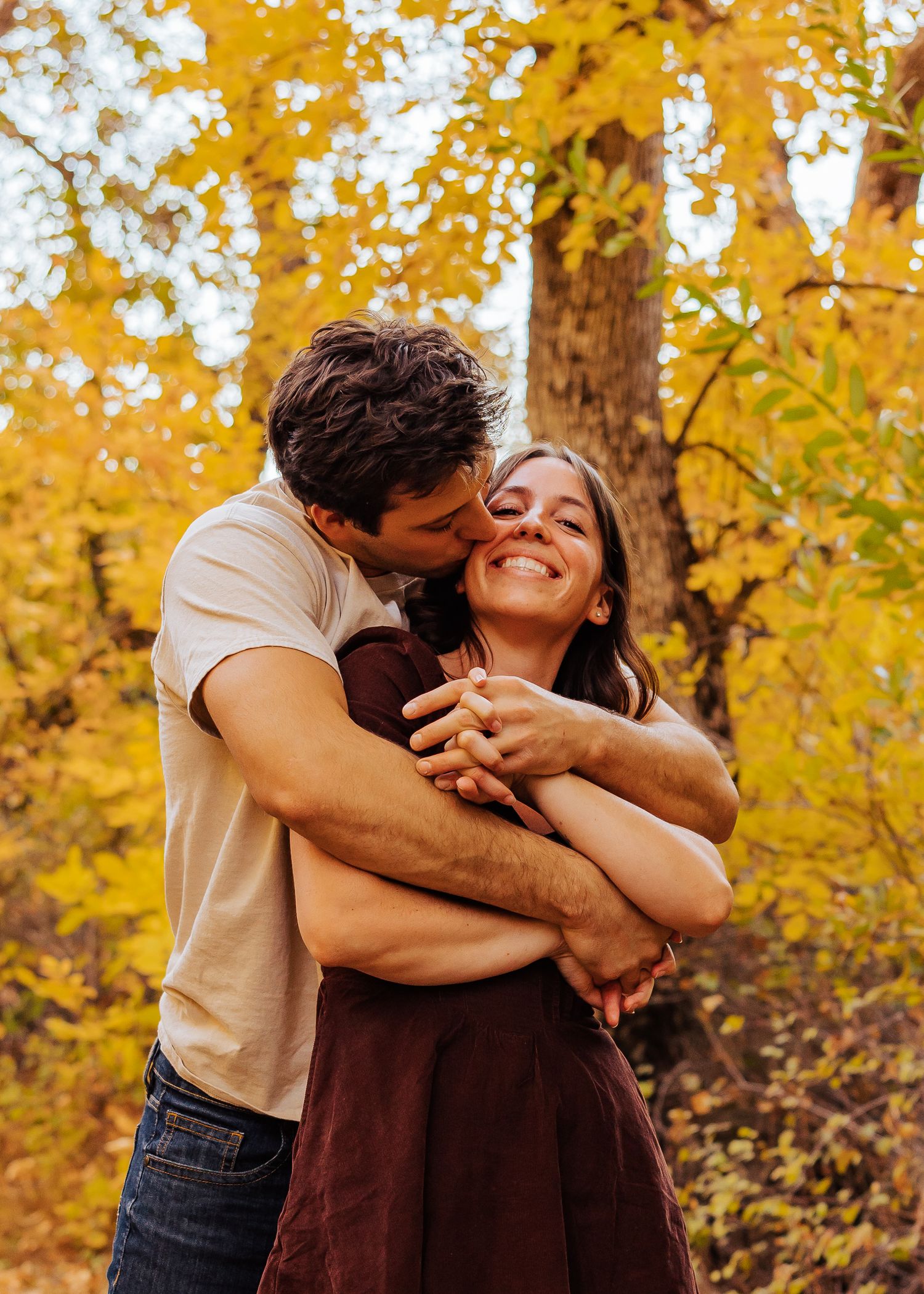 Intimate embrace captured against backdrop of golden autumn trees.