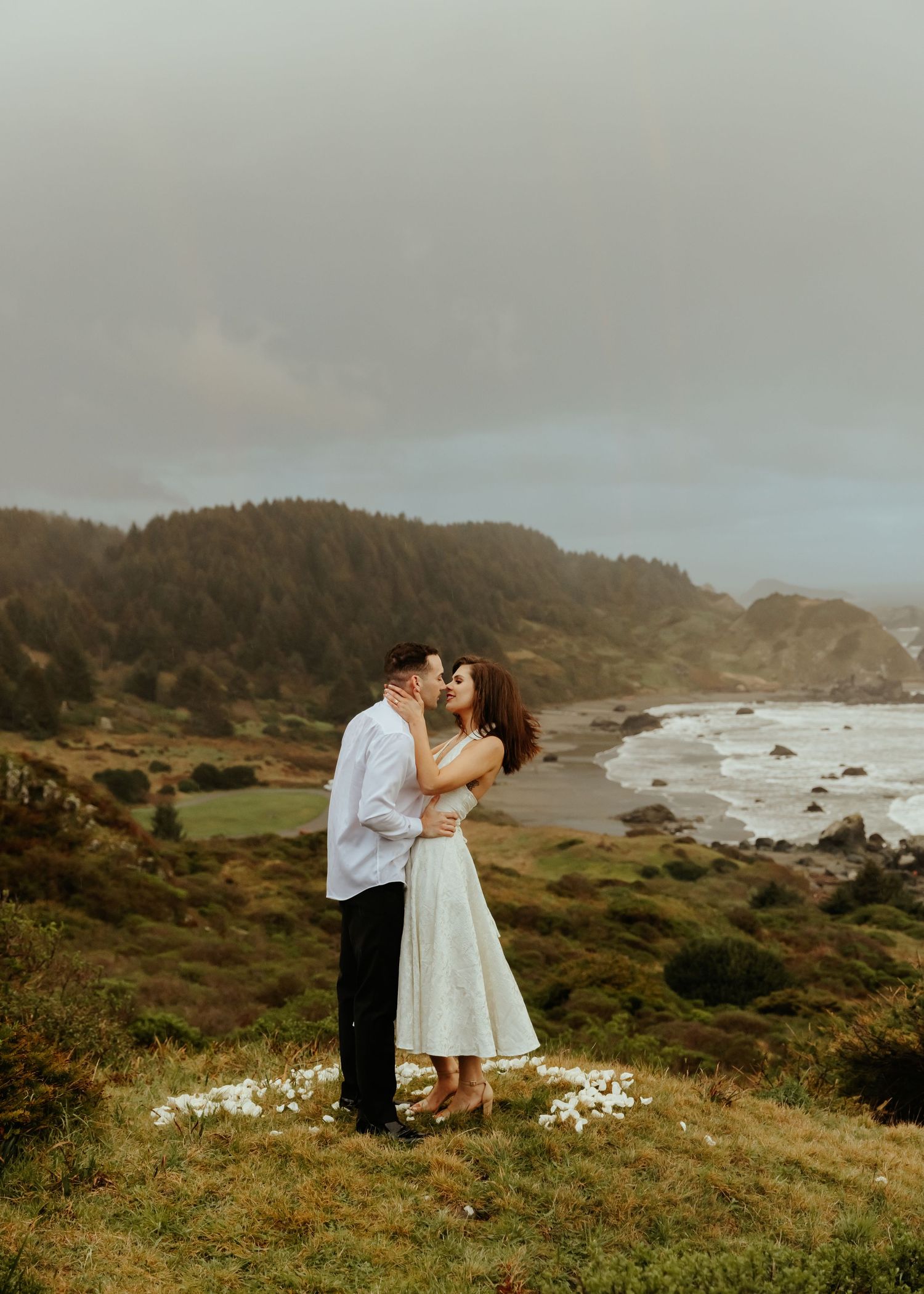 A couple shares a romantic moment overlooking a dramatic rocky coastline.