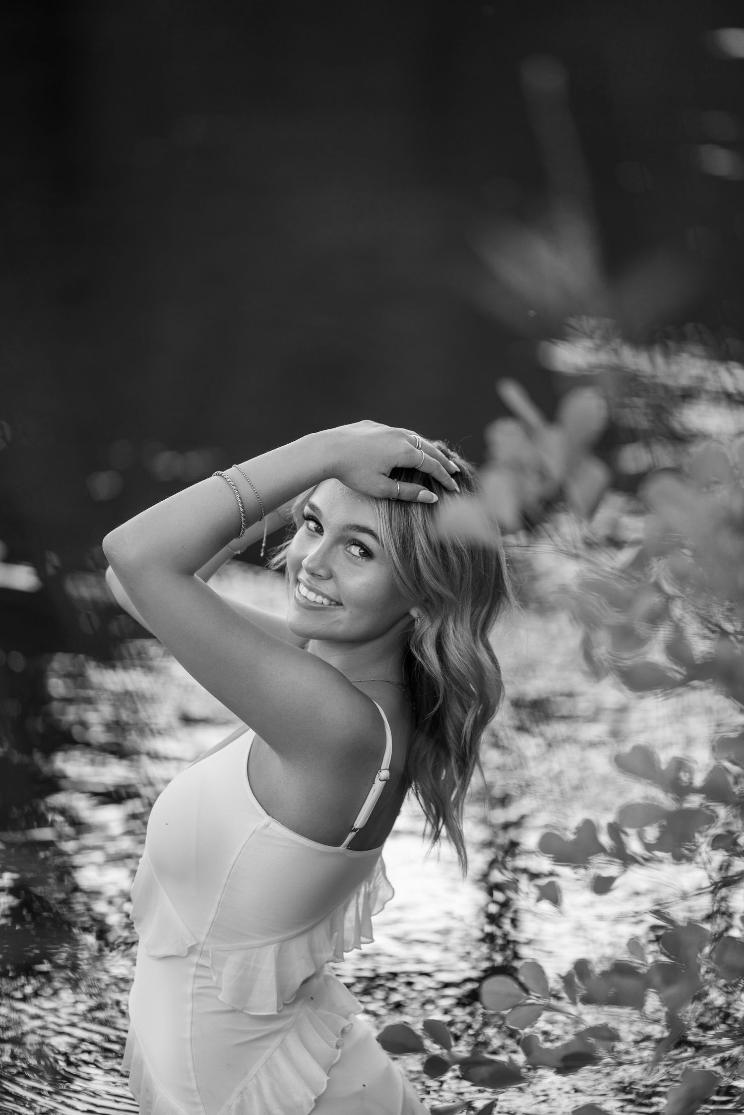 Artistic black and white portrait in white dress with dramatic backlighting near water.