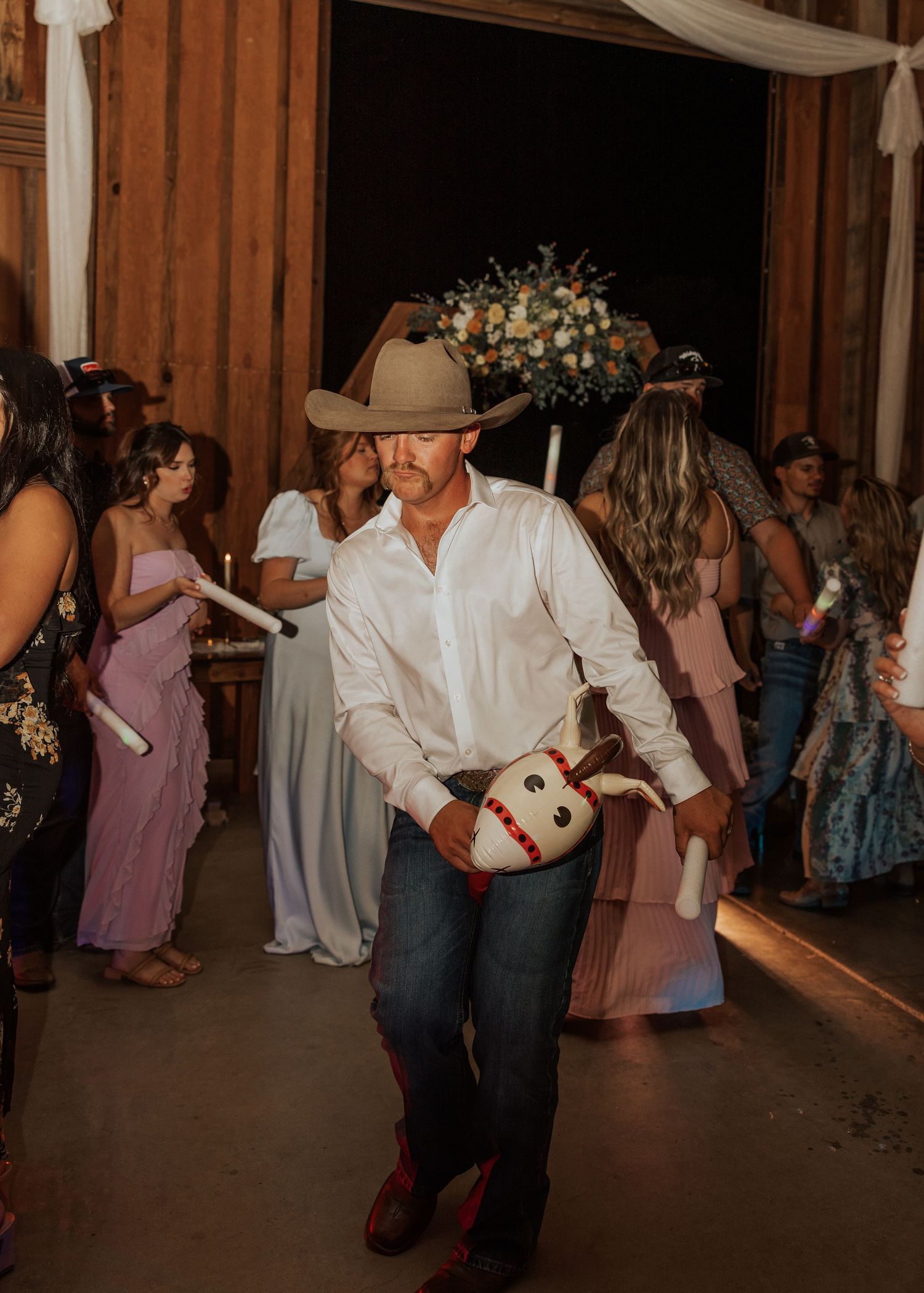 Groom in cowboy hat dancing solo at rustic barn wedding reception.