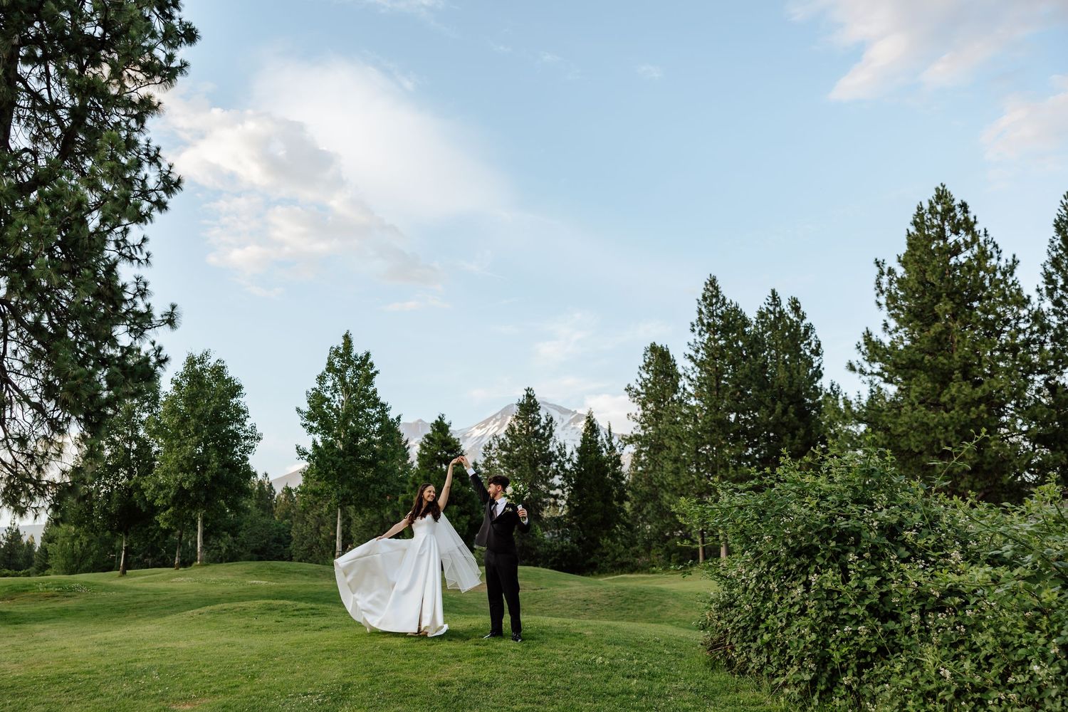 Bride and groom celebrate on a lush golf course surrounded by tall pine trees under a blue sky.